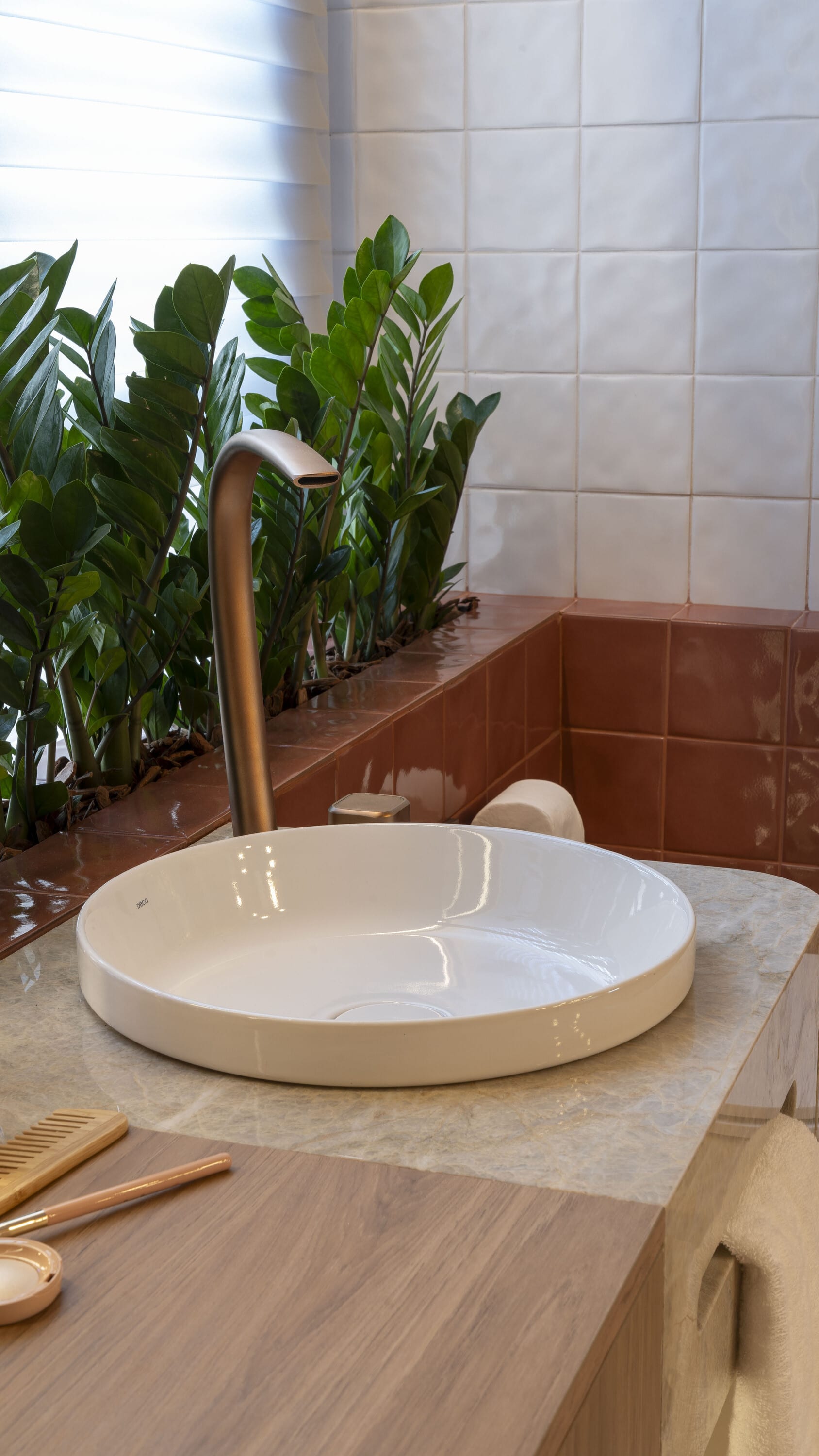 White vessel basin and brass tap on a stone counter beside terracotta tiles and plants
