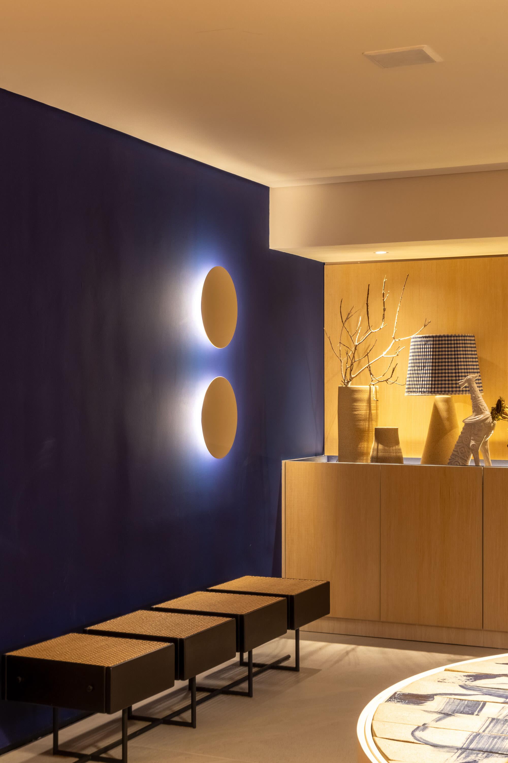 Cobalt blue wall with round backlit sconces above low oak benches