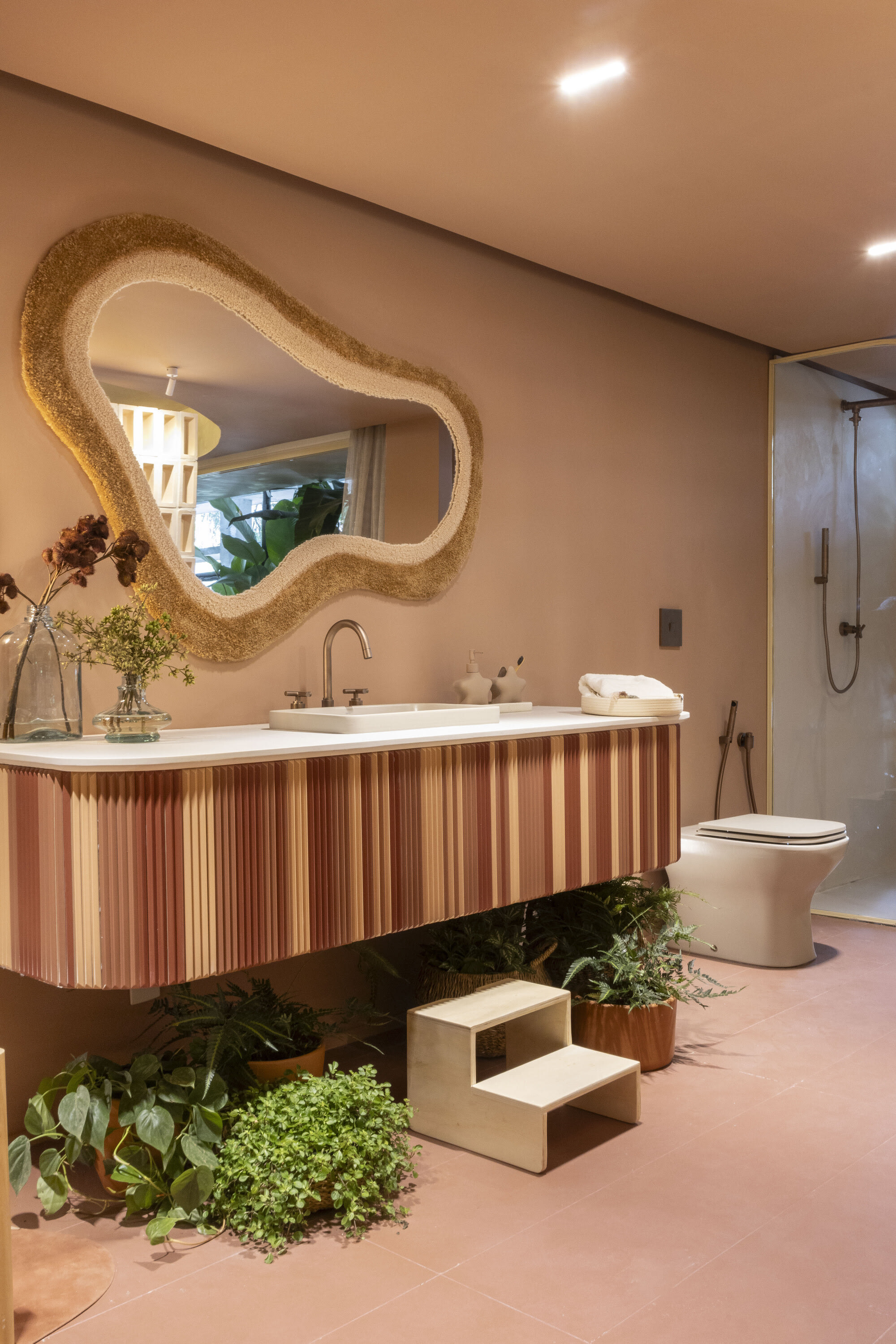 Striped wooden vanity under a wavy cane mirror in a rose plaster kids' bathroom