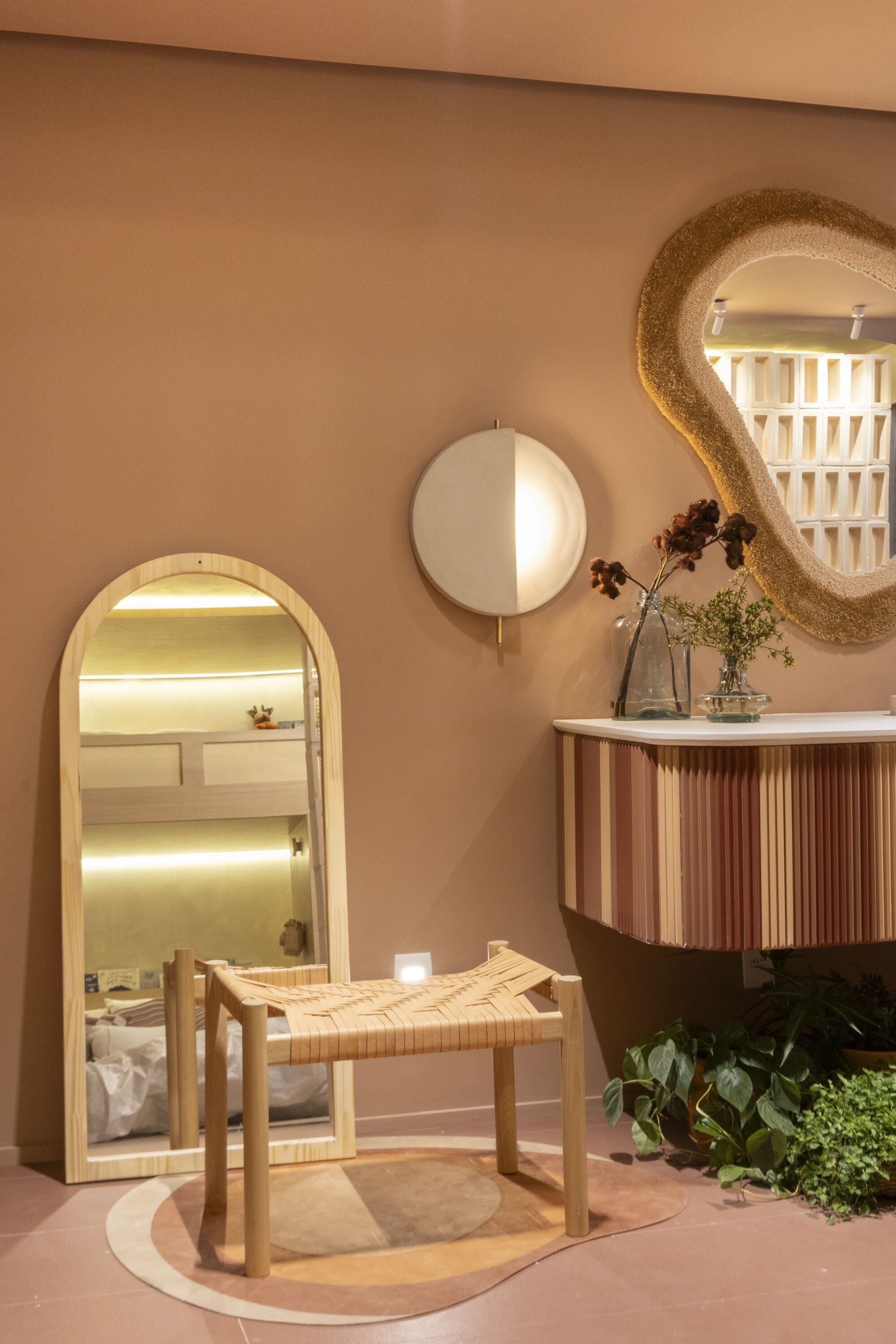 Arched oak mirror, woven stool and round sconce beside a striped vanity