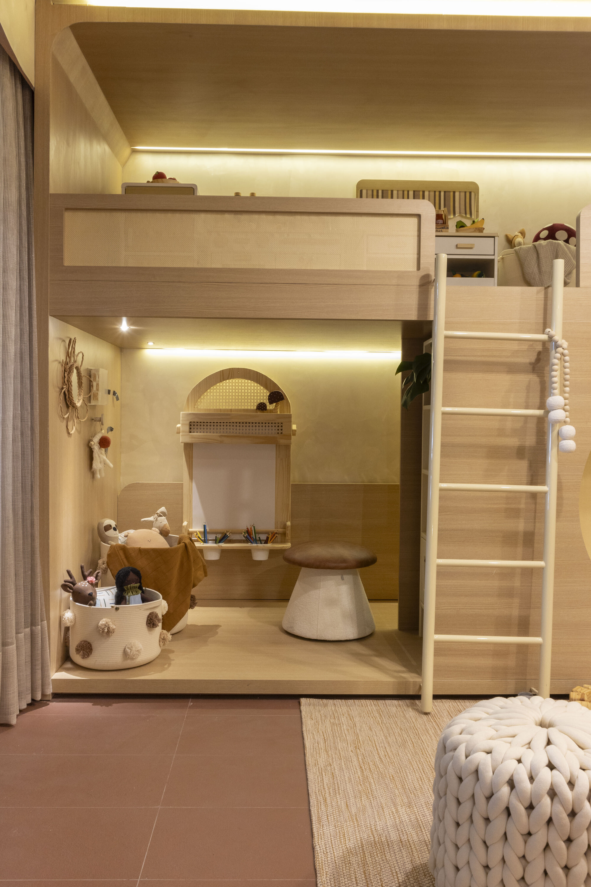 Oak loft bed with a white ladder over a play nook and knitted pouf