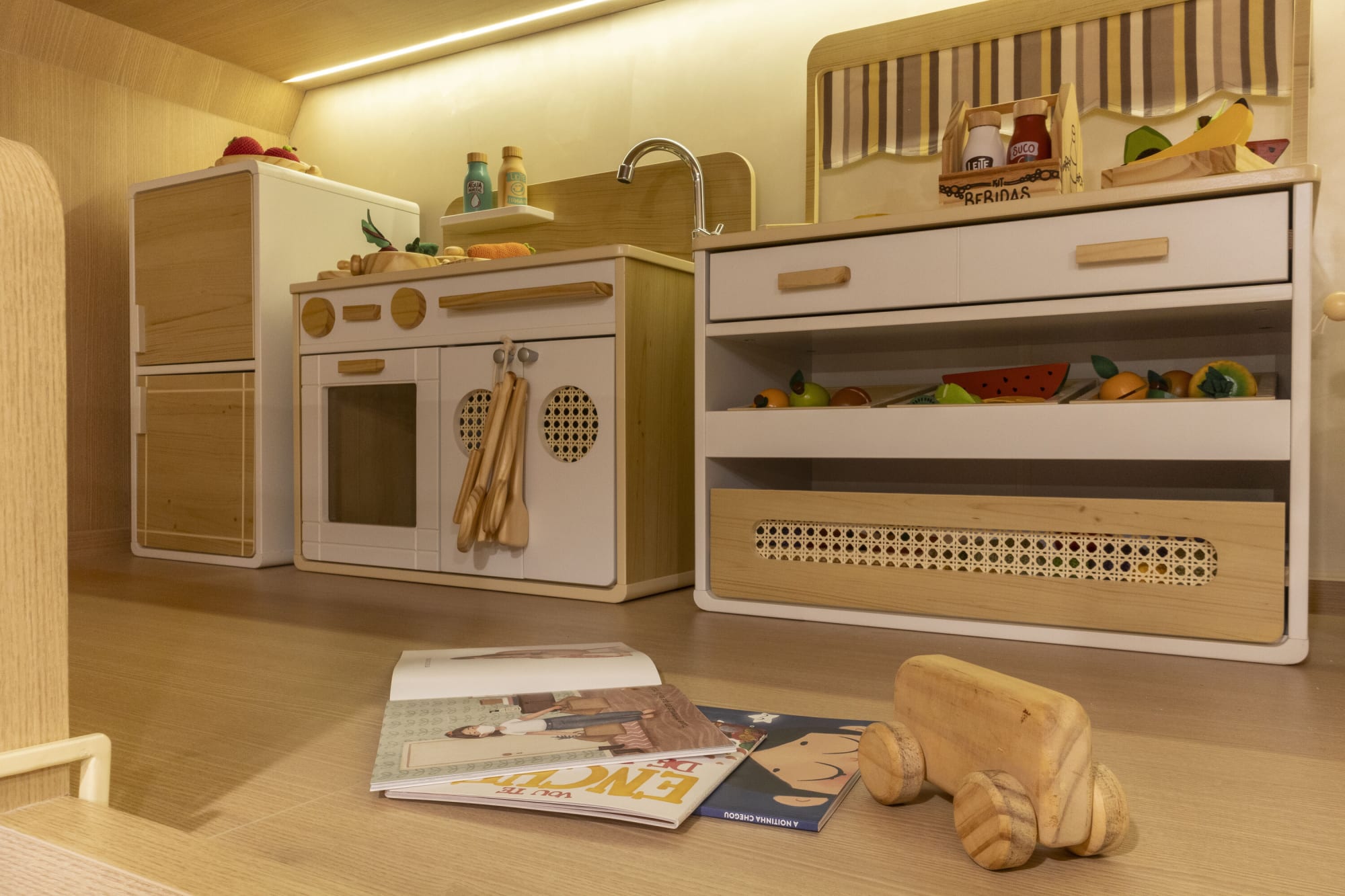 Wooden toy kitchen, cane drawer chest and wooden car on an oak floor
