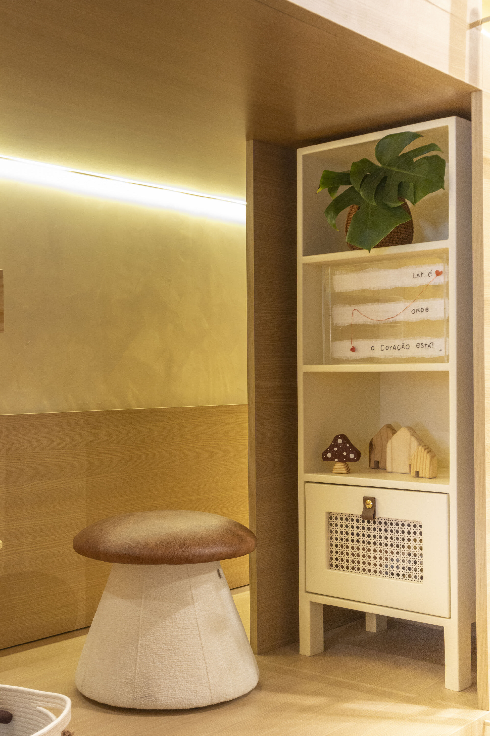 Mushroom stool beside a narrow oak shelf with a plant and small toy houses