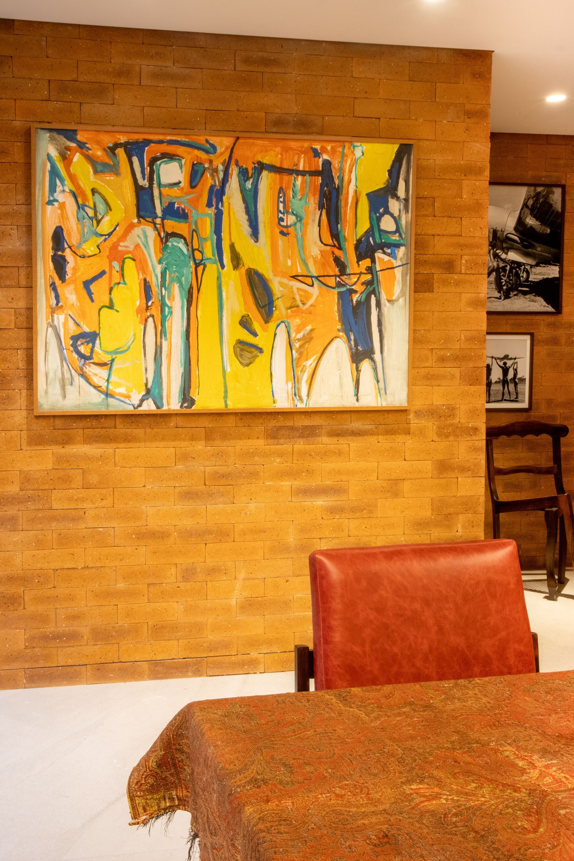 Colourful abstract painting on clay brick above a red leather chair and paisley tablecloth