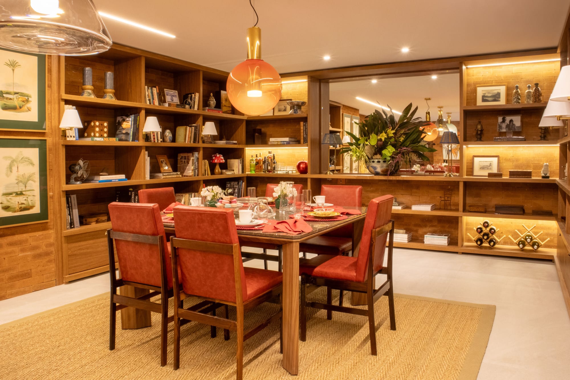 Red leather dining chairs around a set table surrounded by lit oak shelving