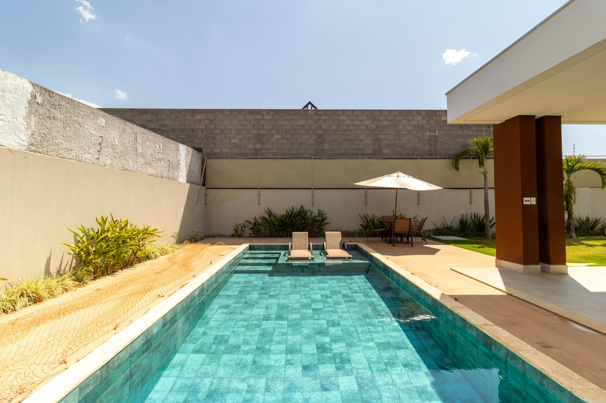 Long green tiled pool with sun ledge beside a rust column and lawn