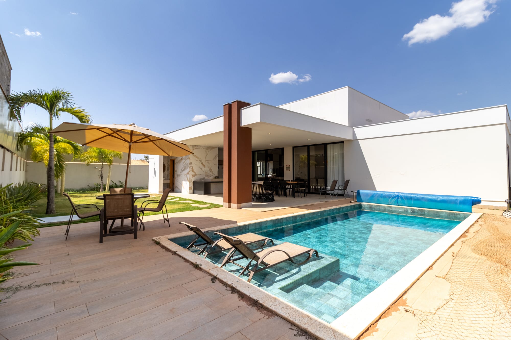 Single storey white house beside a pool with parasol and loungers