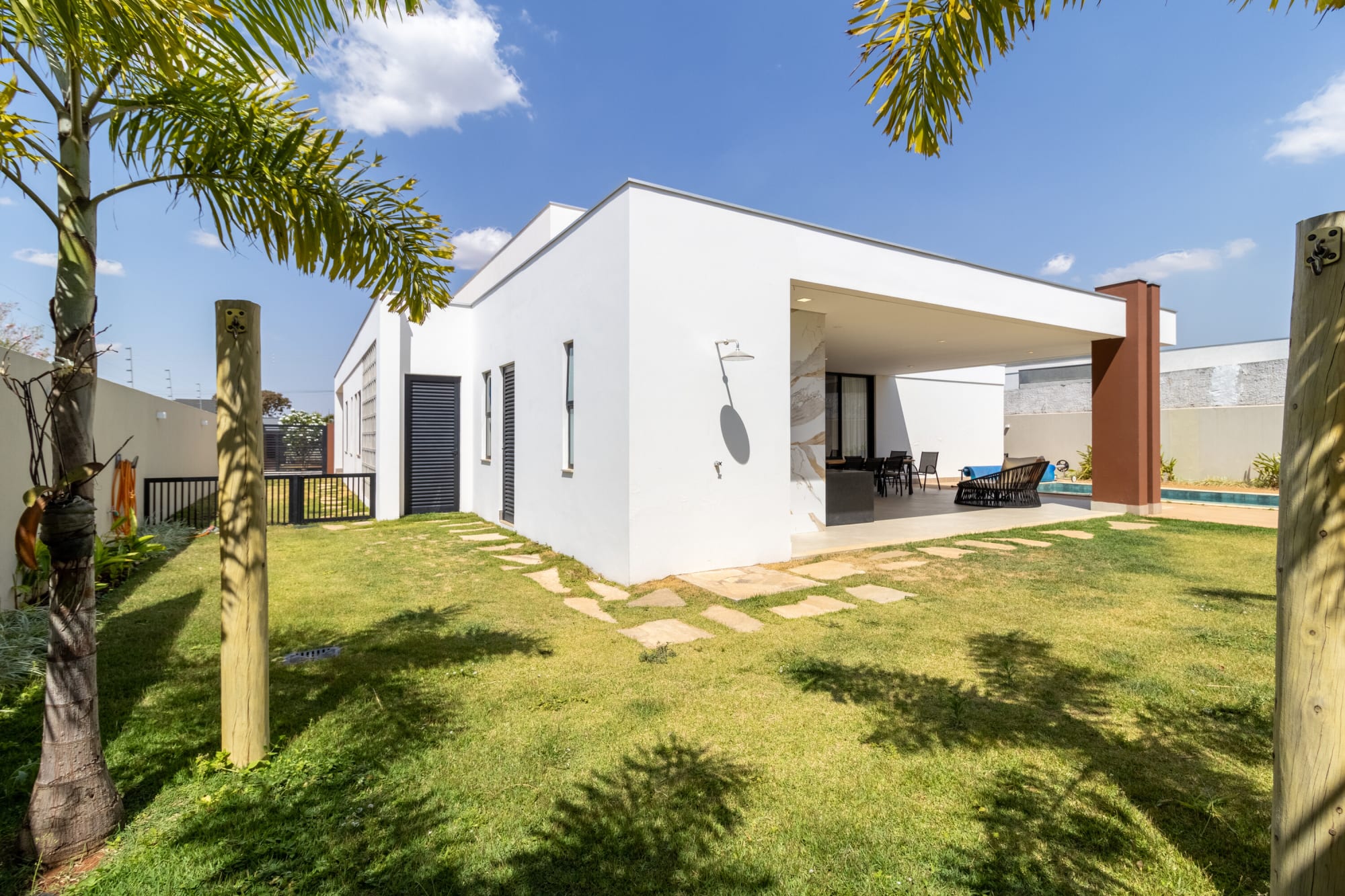 Lawn with stepping stones leading to a white single storey house and palms