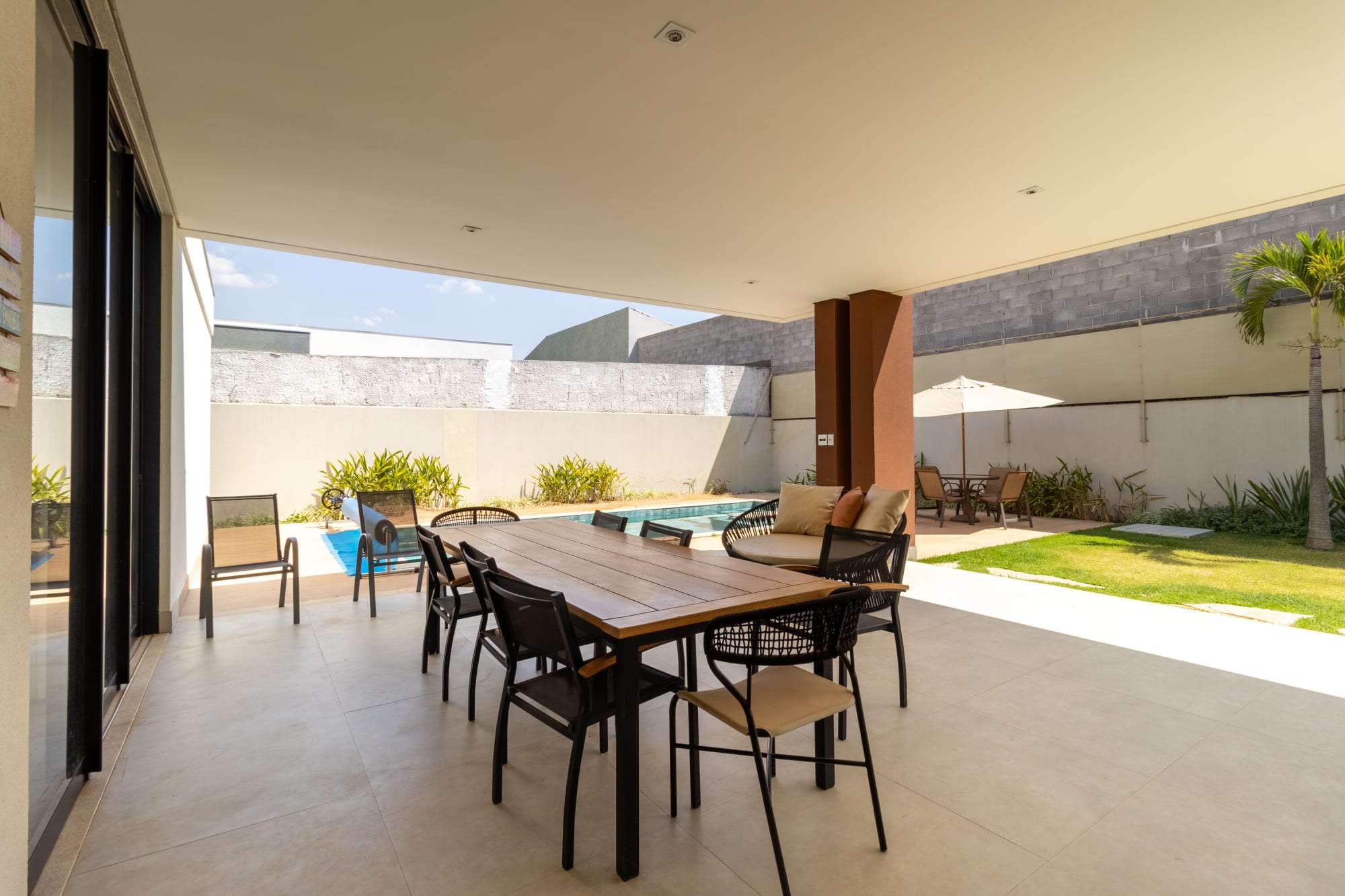 Covered terrace with timber dining table and black chairs facing the pool