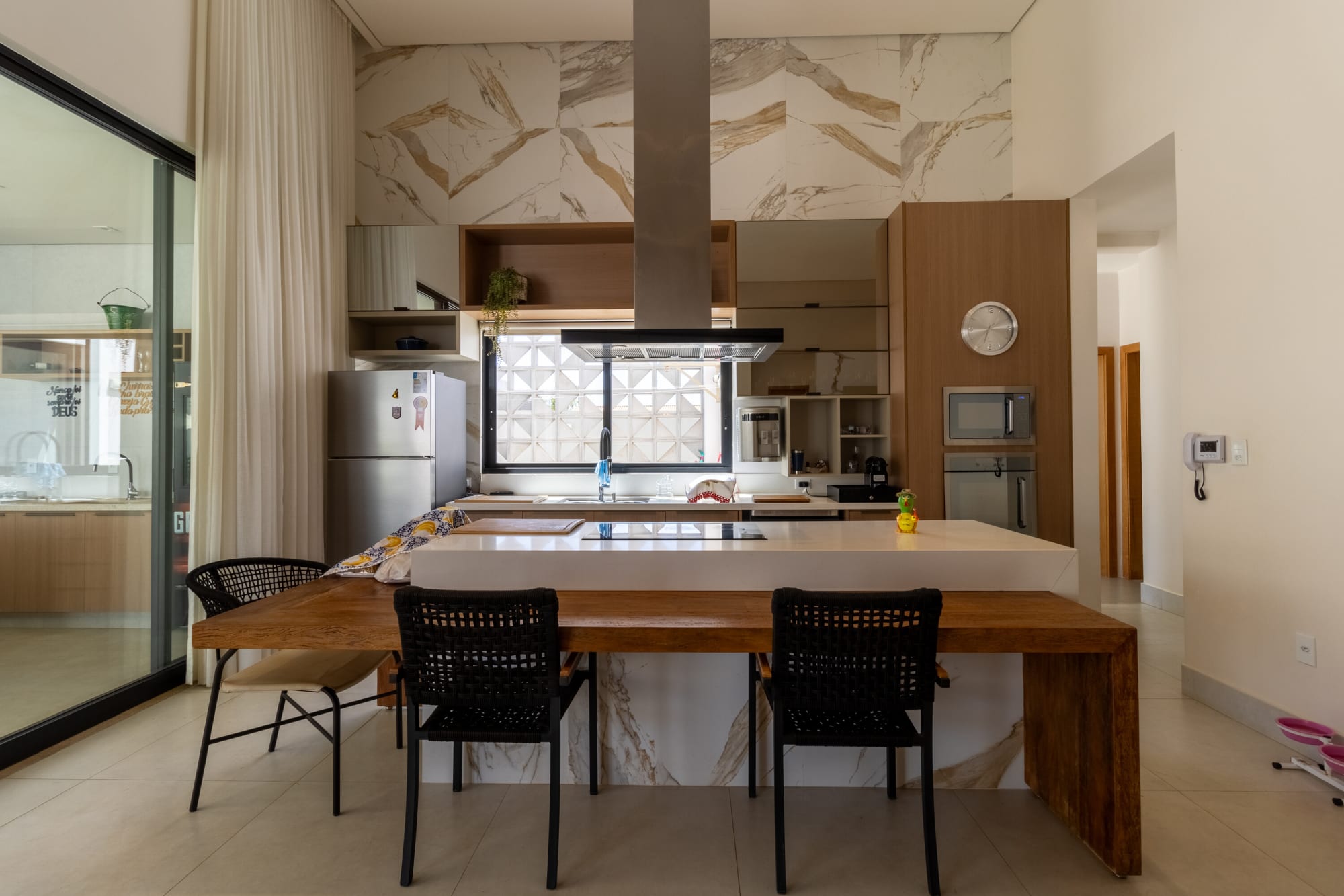 Kitchen with marble veined island, steel hood and black chairs at a timber bar