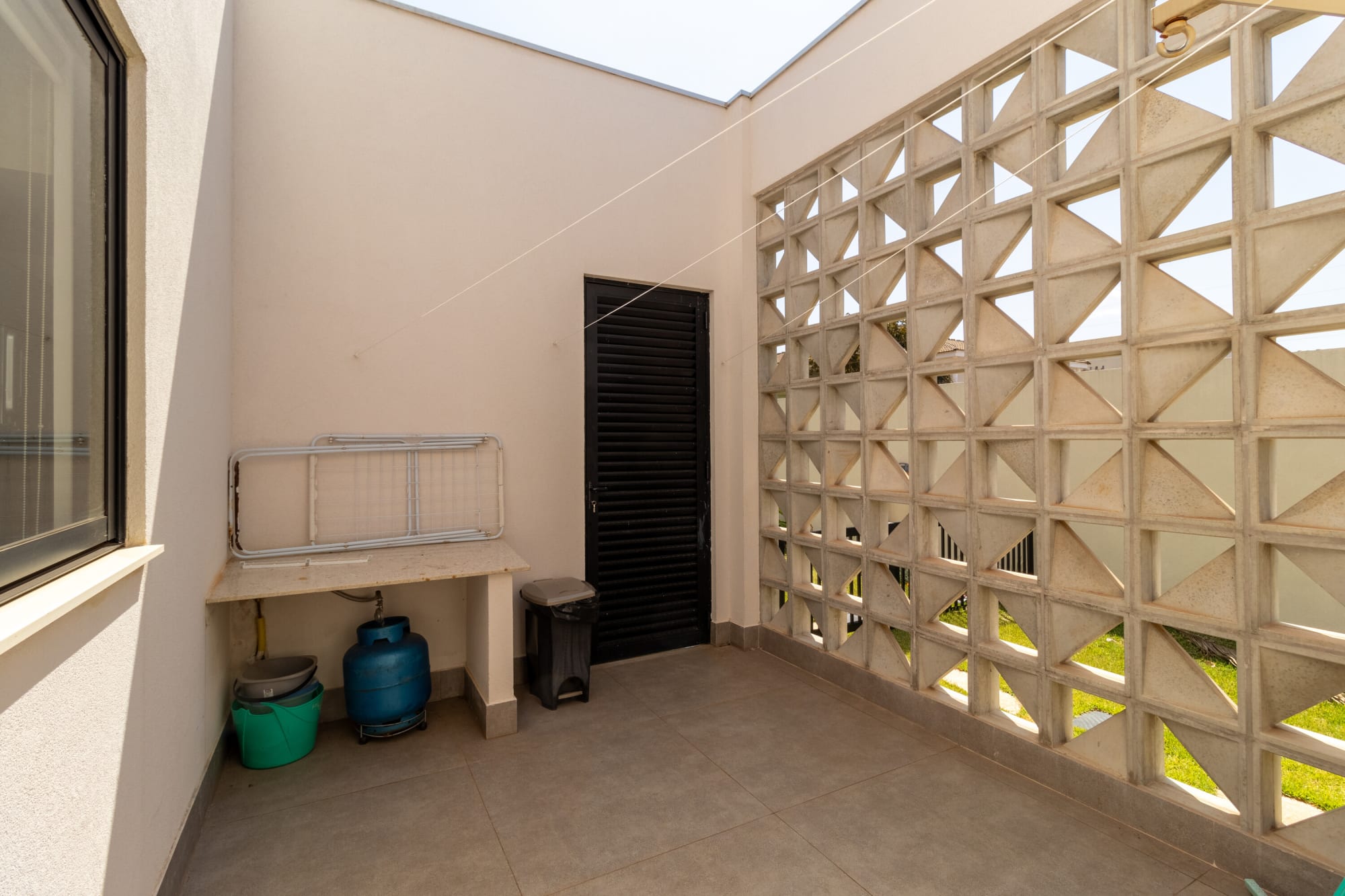 Service yard with cobogó block wall, laundry tank and black door