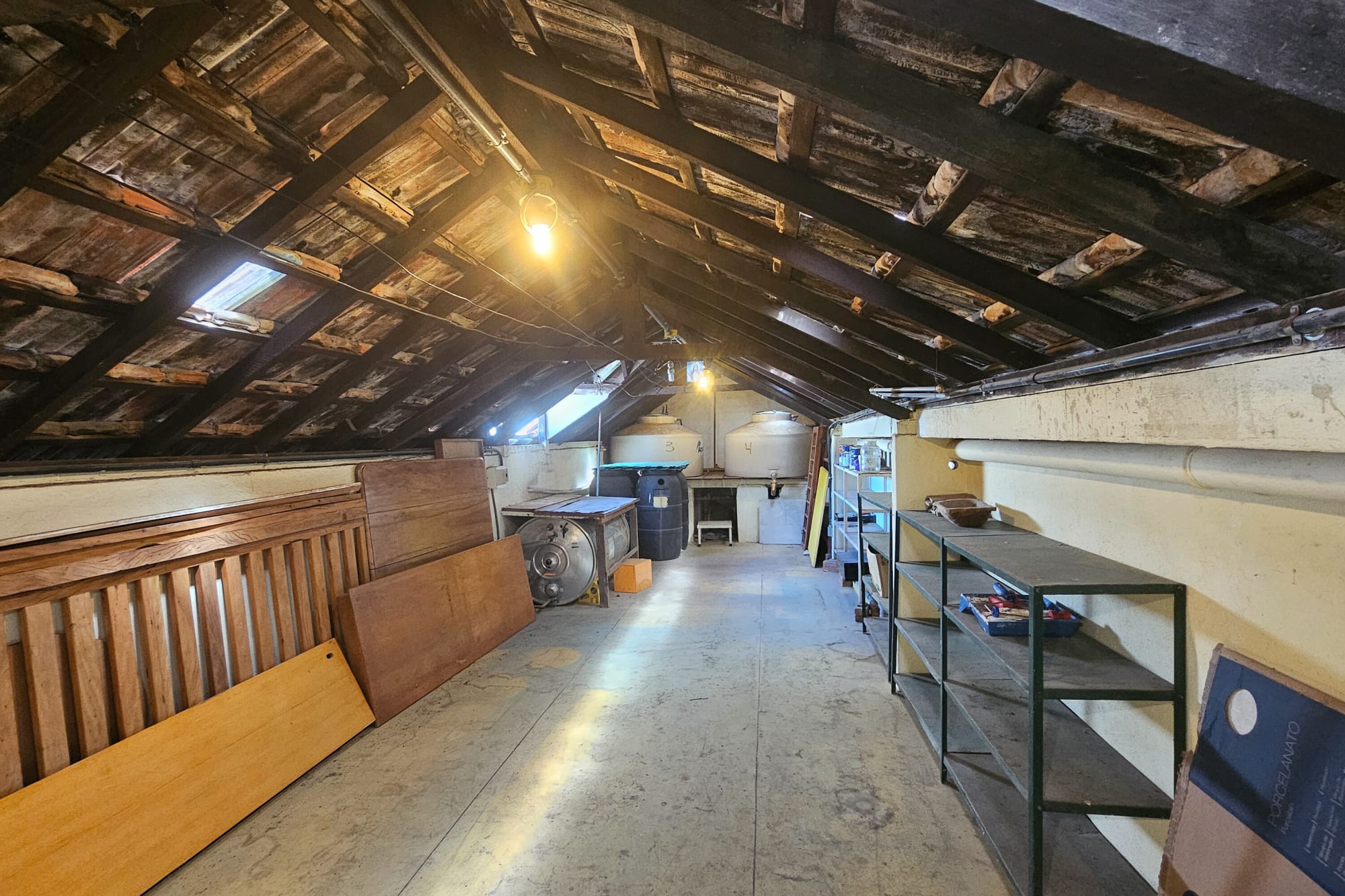 Attic under exposed clay tile roof with timber beams and steel shelving