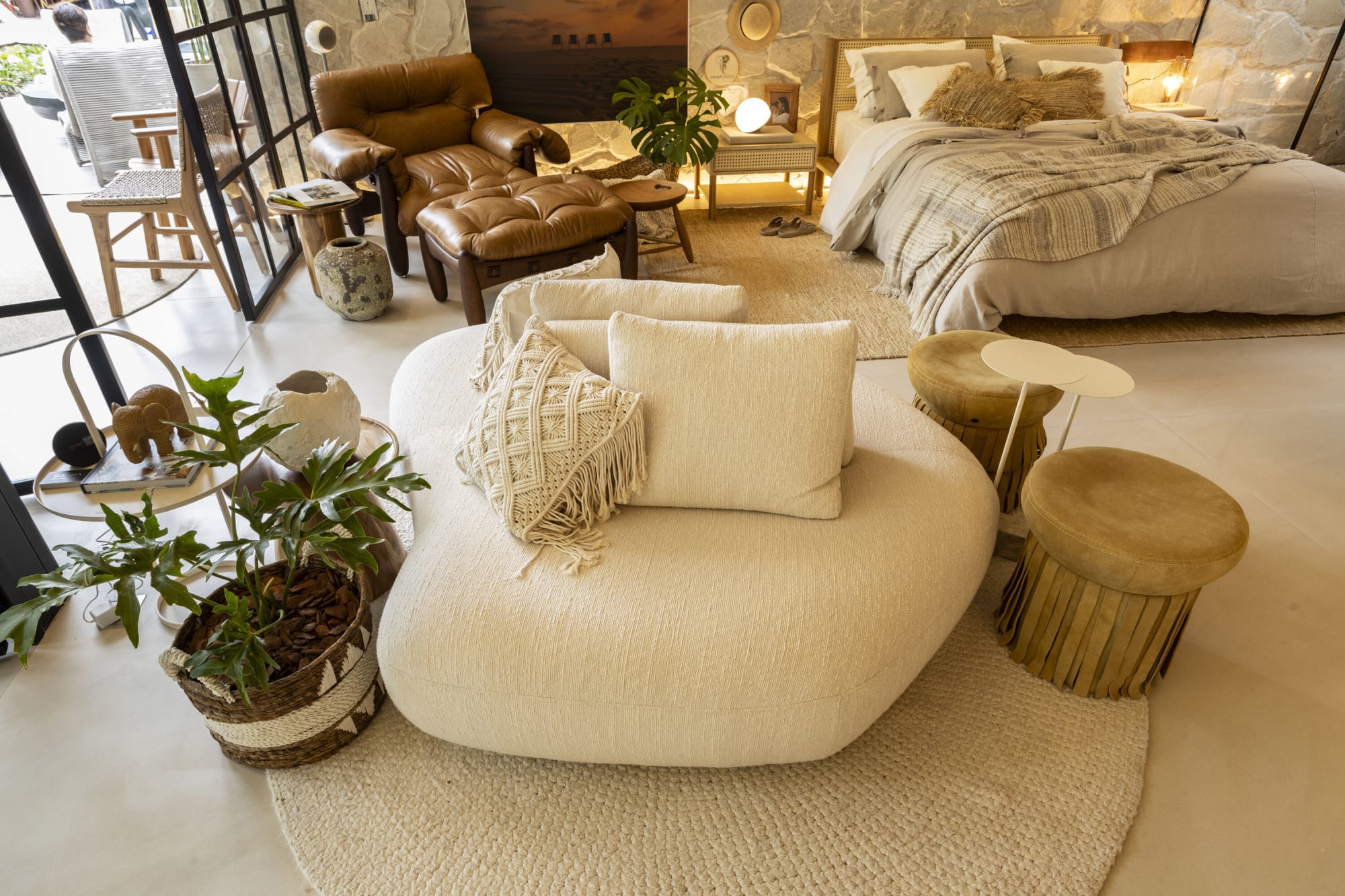 Sofá curvo crema y bancos de madera junto a una cama y un sillón de piel