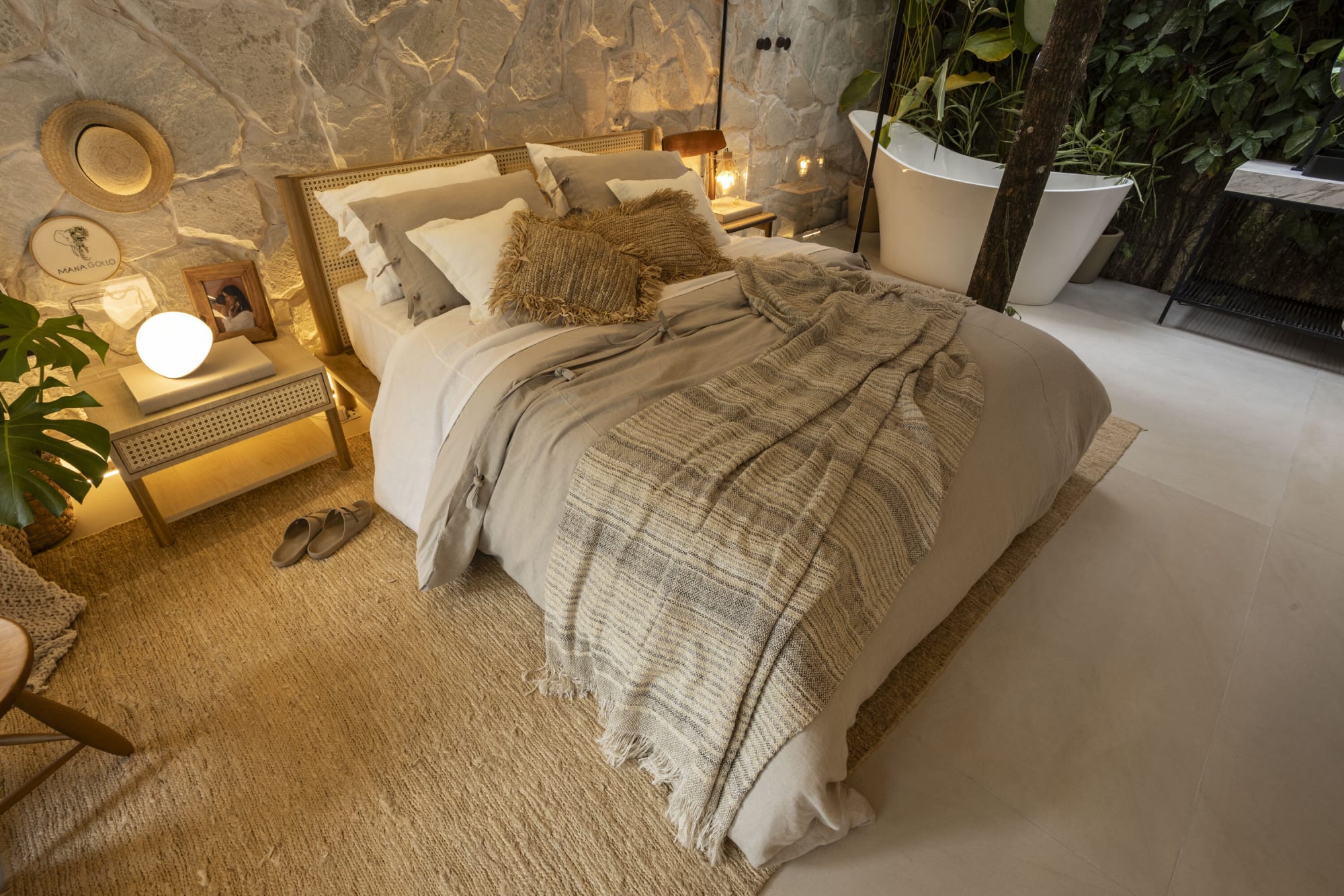 Cama con manta de cuadros y una tina exenta detrás junto a un muro plantado