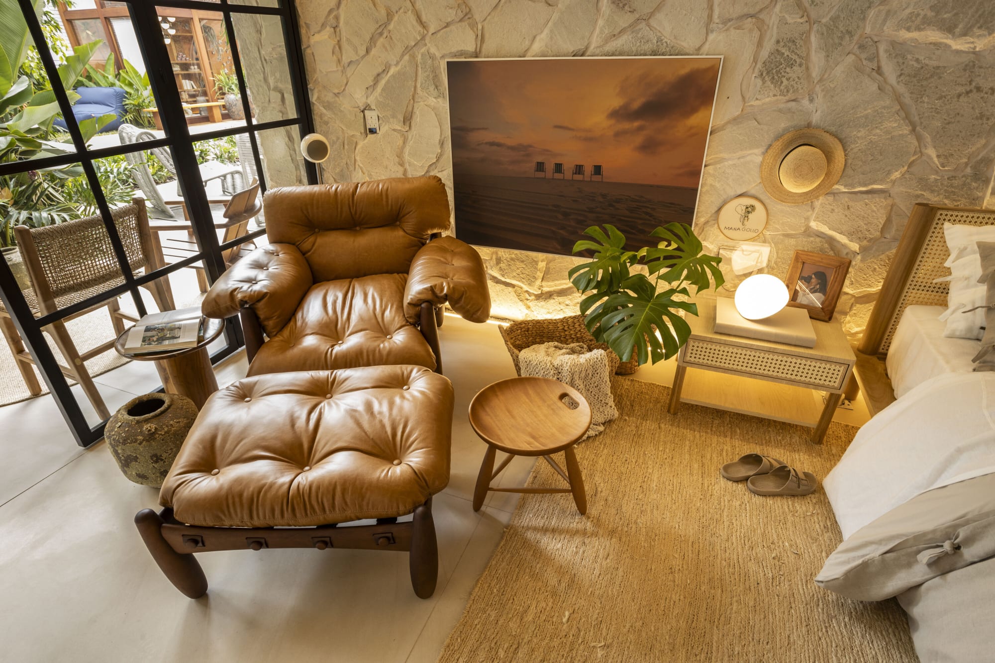 Sillón de piel y reposapiés junto a un buró frente a un muro de piedra