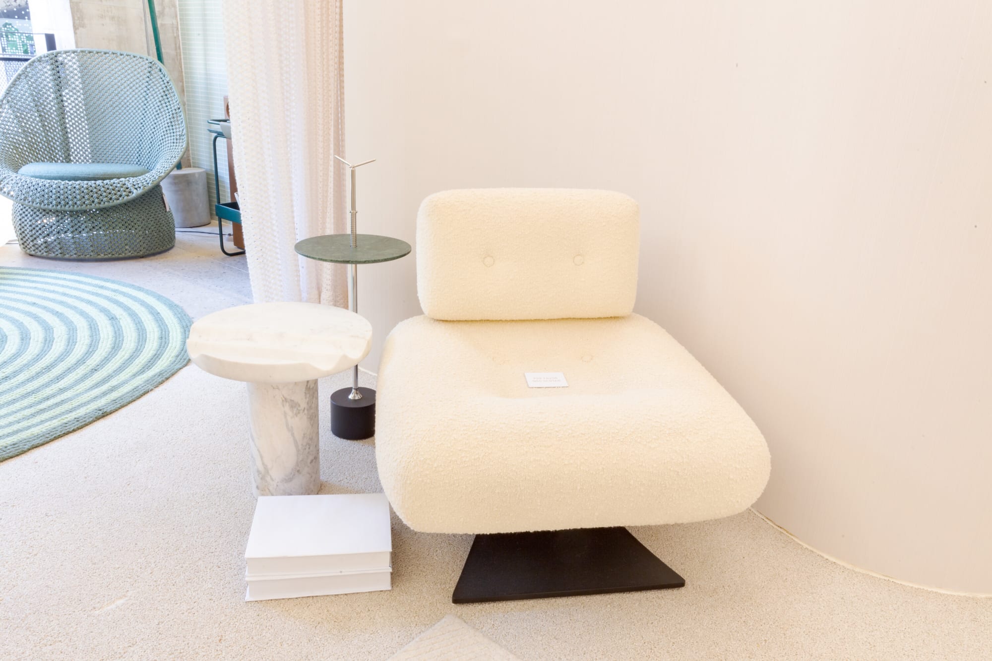 White curved chaise and marble side table beside a sheer curtain on a pale floor