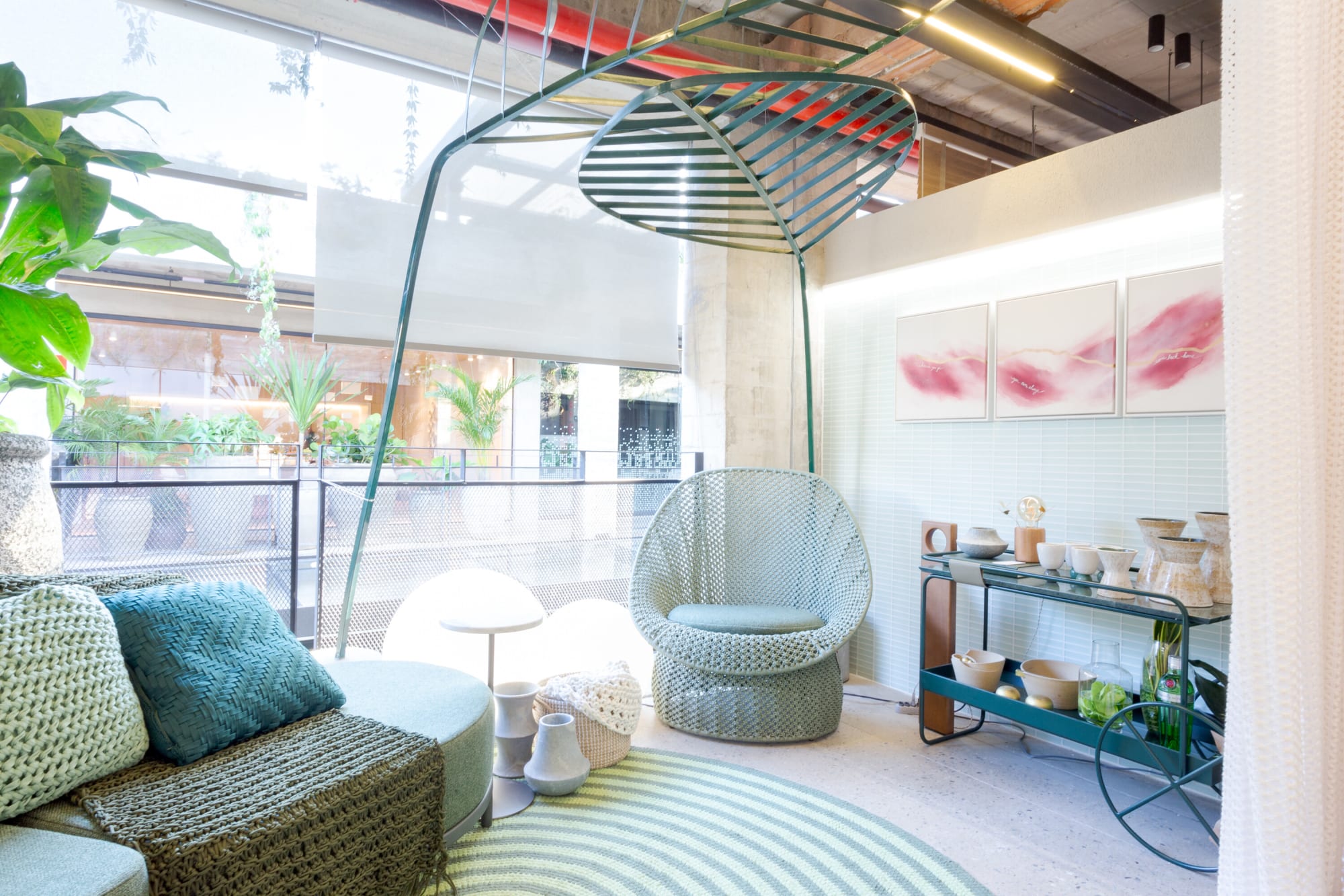 Woven egg chair, sage sofa and a serving trolley with pink artworks behind