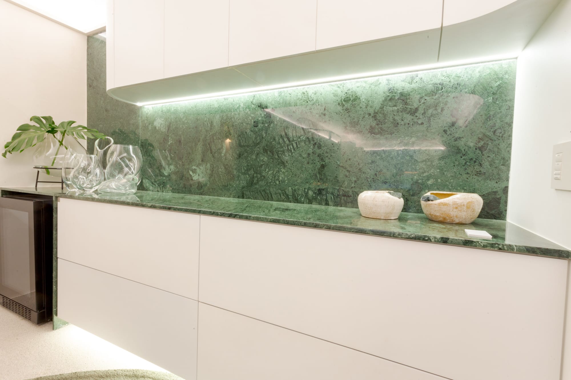 Green marble splashback and counter with white cabinets and under cabinet lighting
