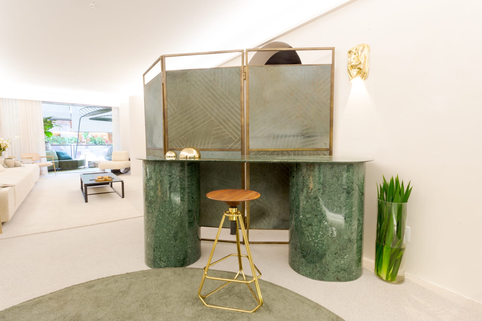 Green marble console with brass screen and a gold stool on a round green rug
