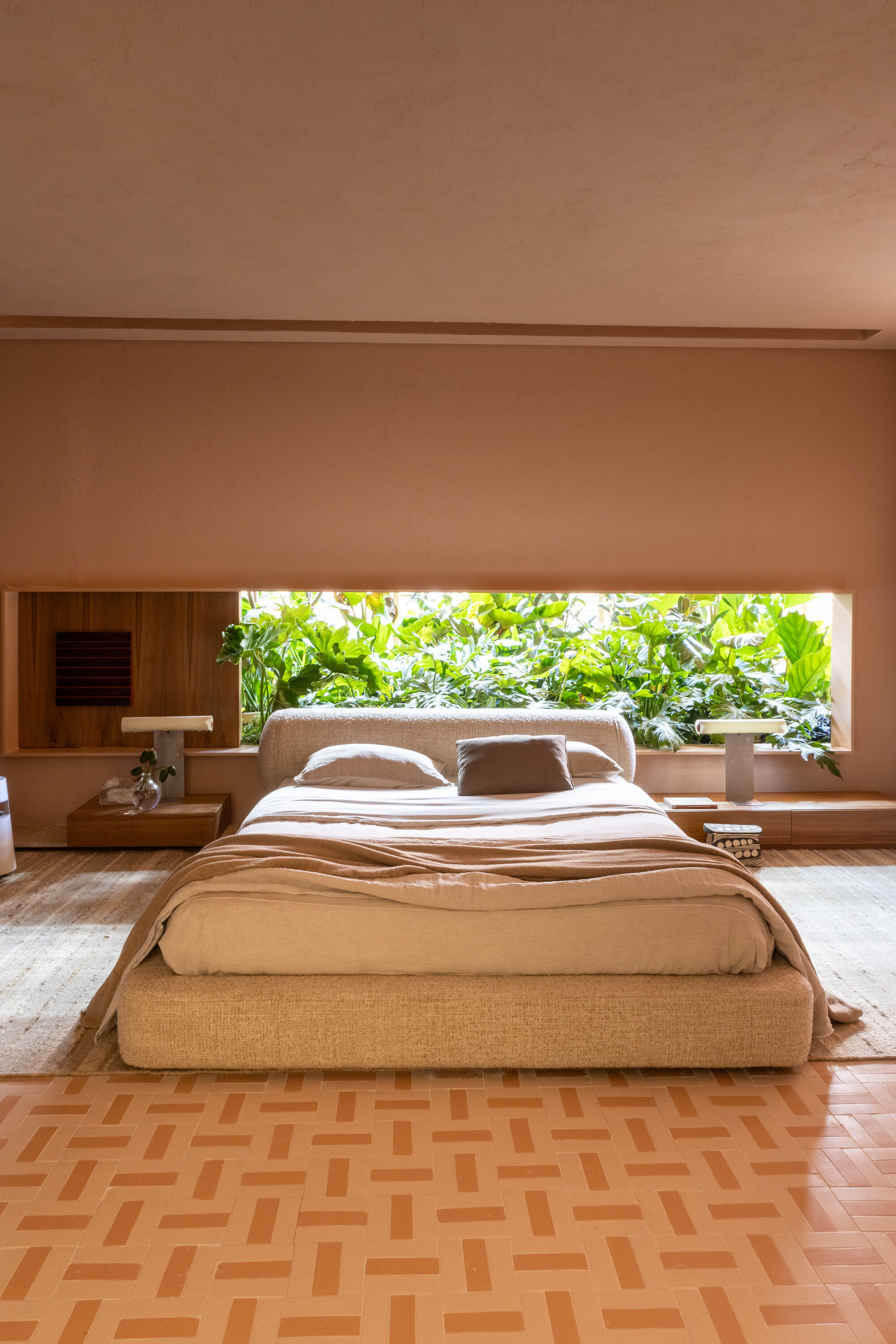 Upholstered bed facing a long garden window in a terracotta toned bedroom