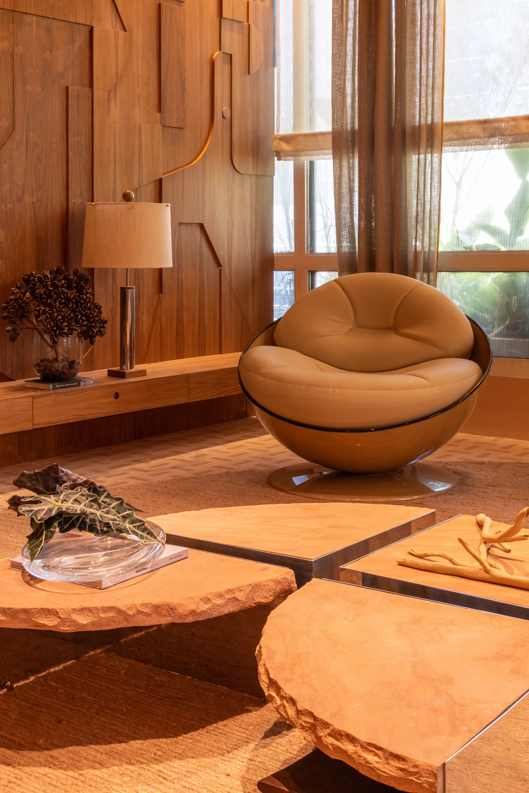 Round leather armchair and carved stone tables before a relief panelled timber wall