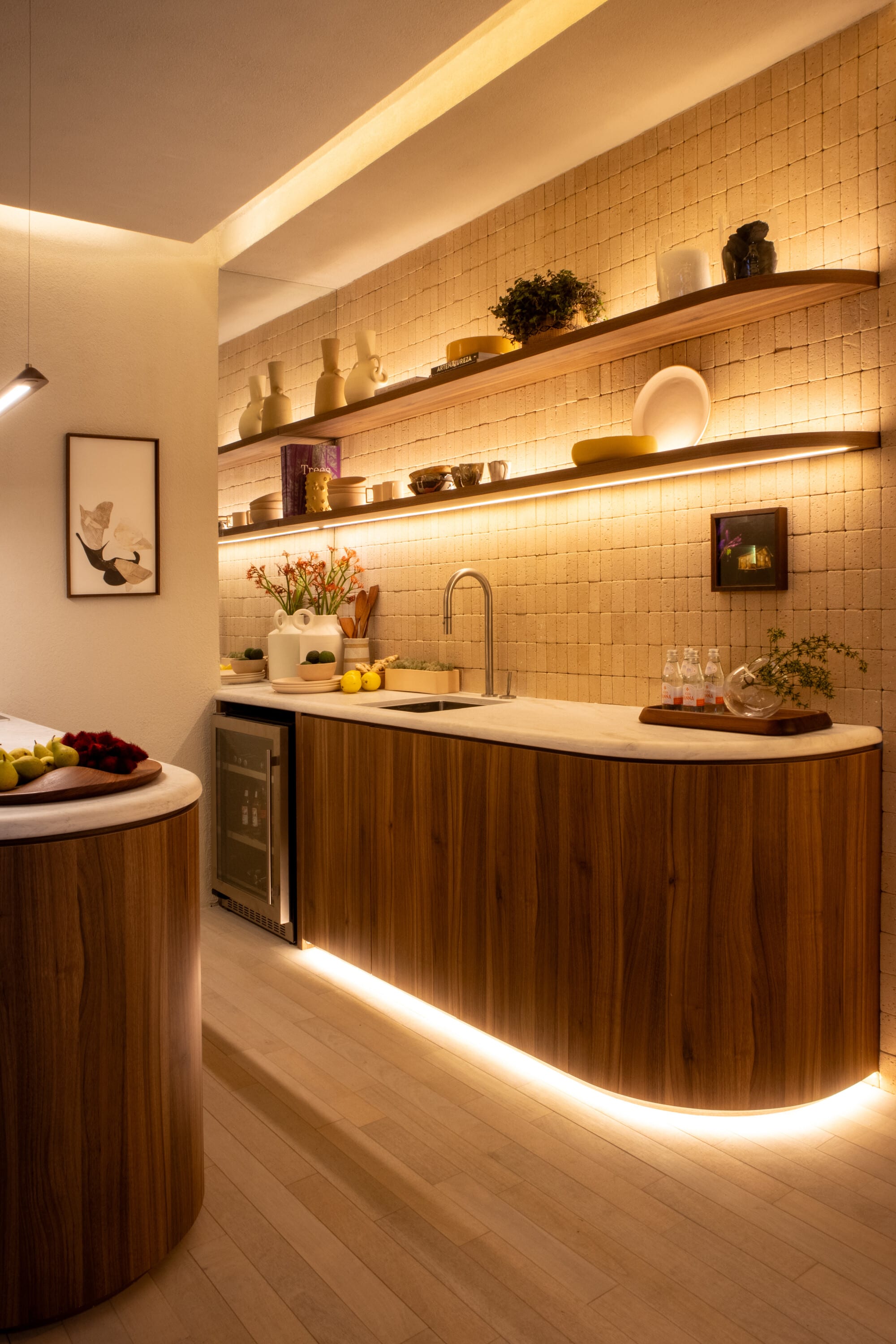 Curved walnut kitchen counter with lit shelves of ceramics and a tiled splashback