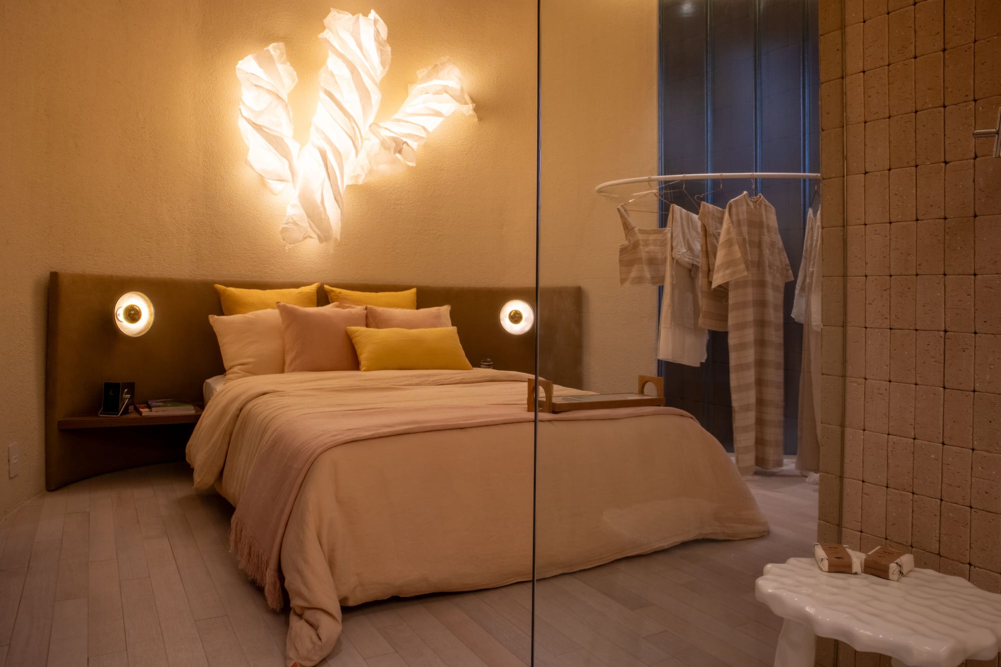 Bedroom with pink bedding beside a glass partition and a rail of hanging linen