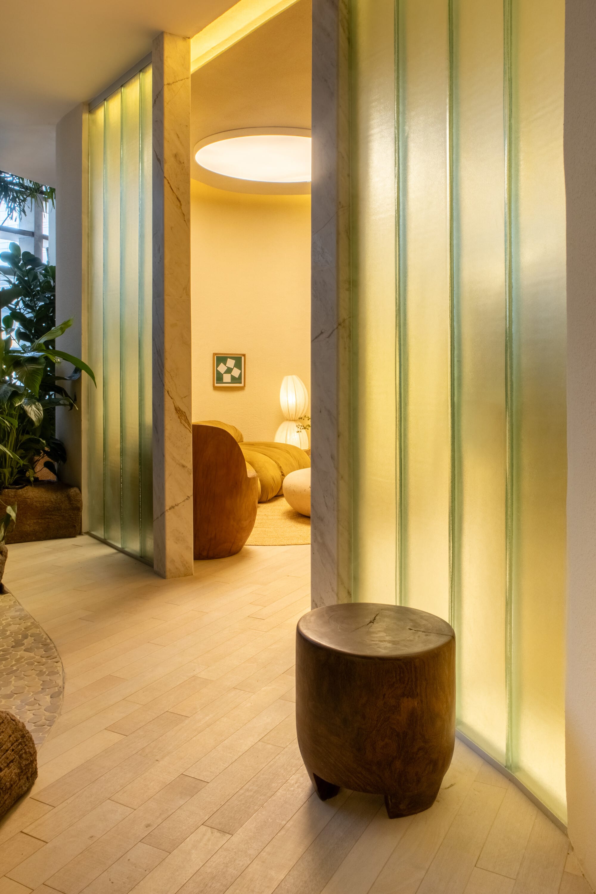 Ribbed glass panels lit from within beside a round timber stool in the tiny house