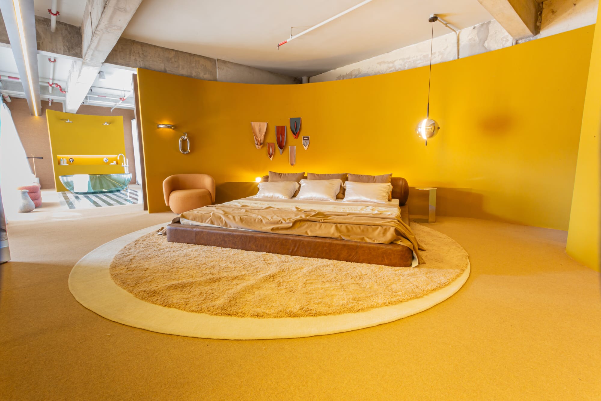 Leather bed on a round cream rug inside a curved saffron wall under a concrete ceiling