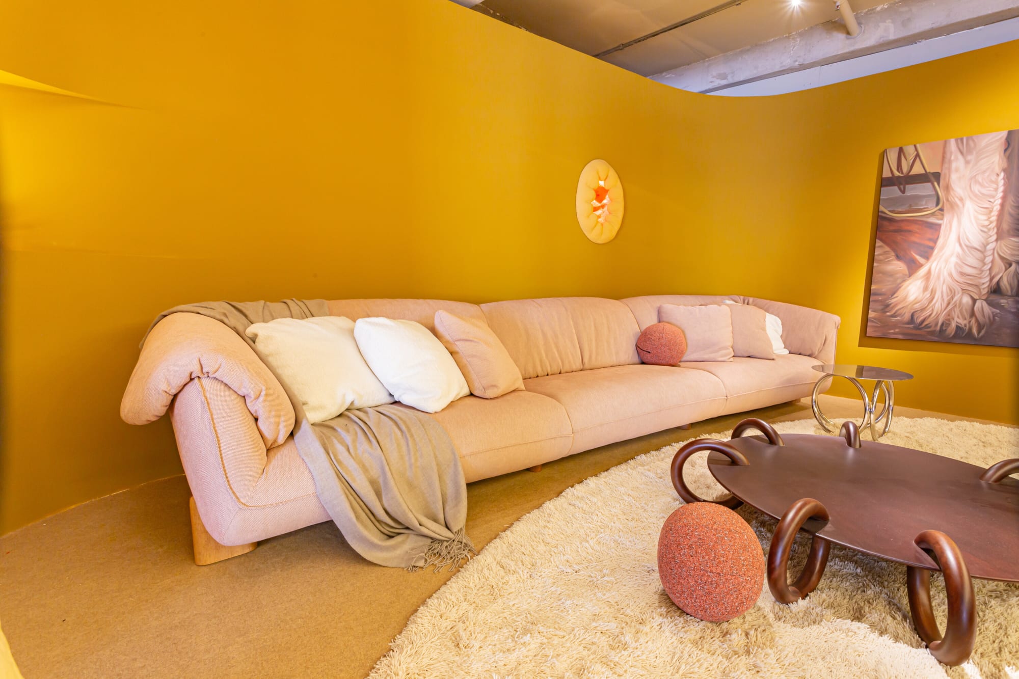 Pink sofa with cushions and throw beside a ring legged table on a cream shaggy rug