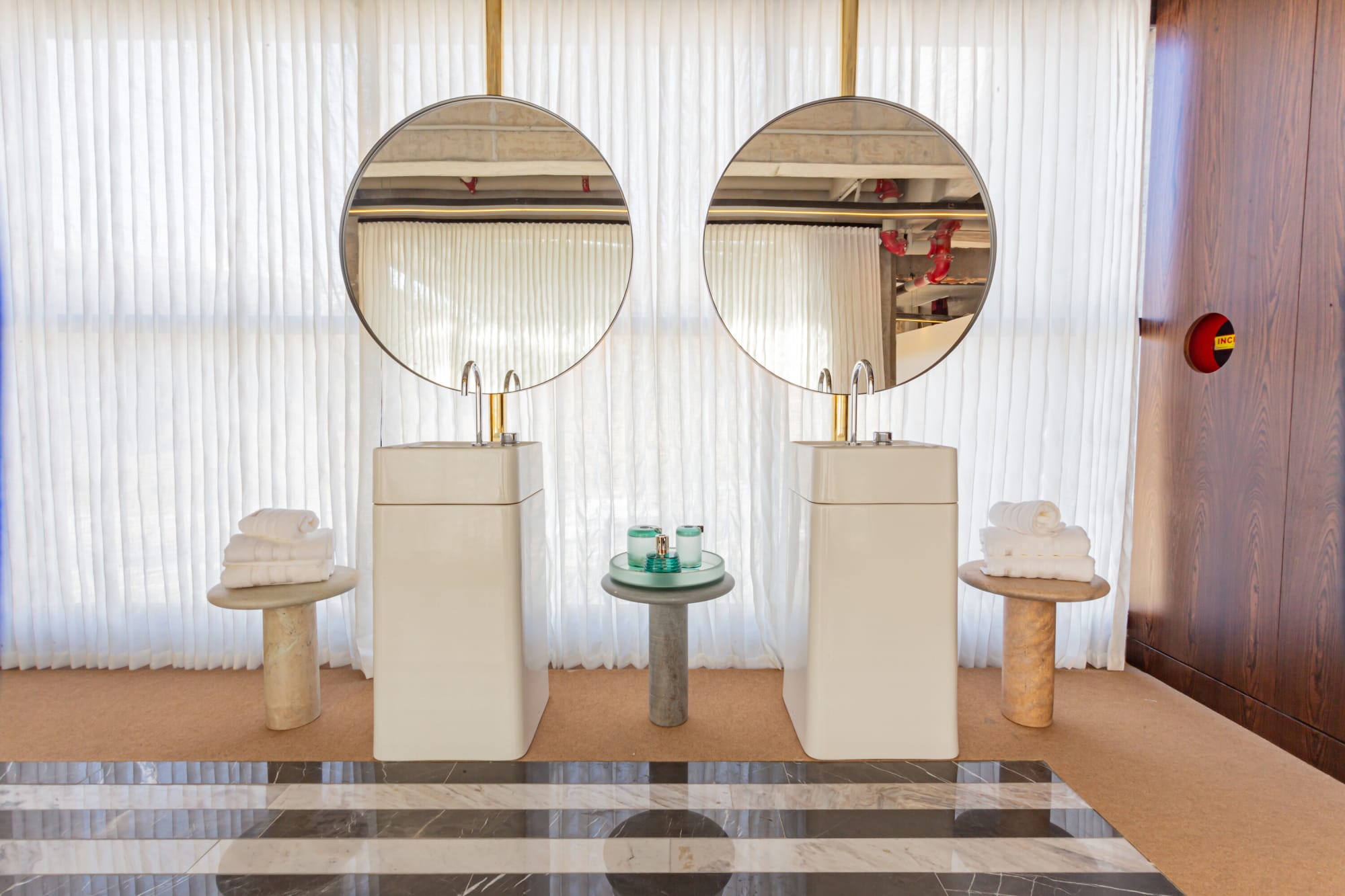 Twin white pedestal basins under round mirrors with towels on striped marble