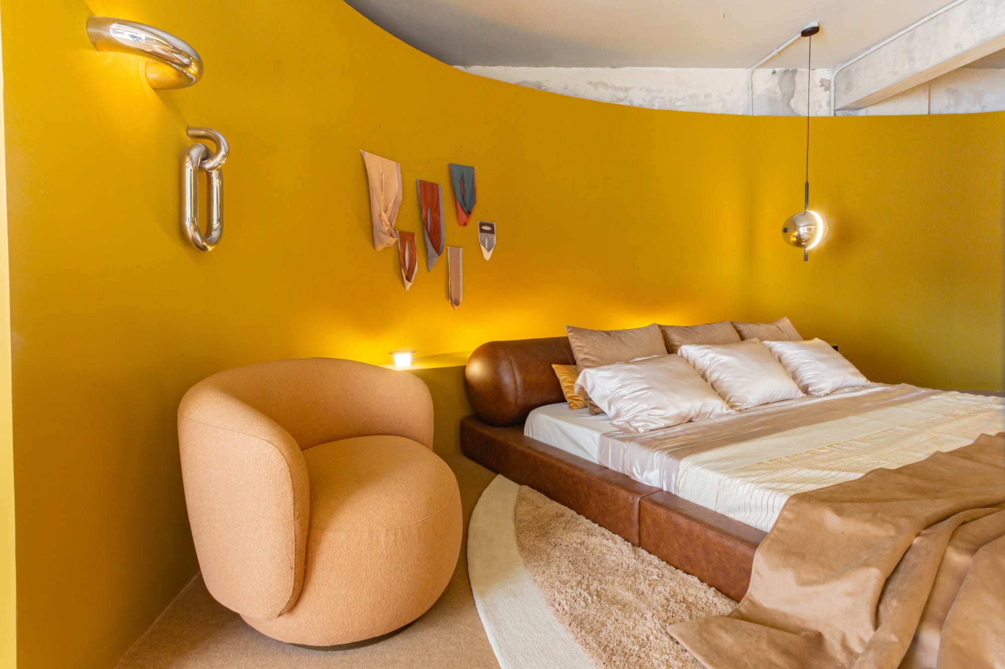 Peach armchair beside the leather bed under a pendant lamp and wall objects on saffron