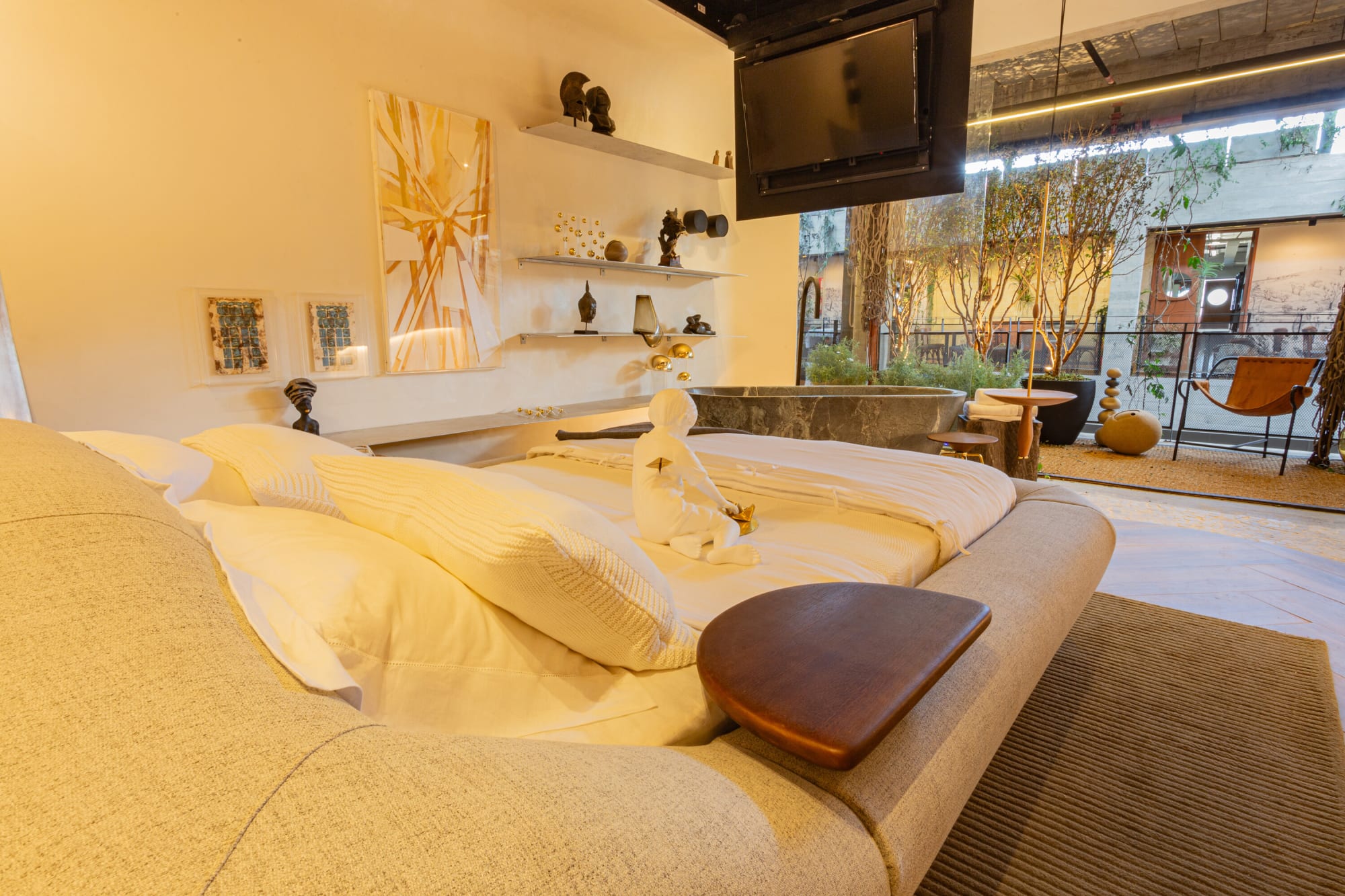 Upholstered curved bed with white linen and a leather side tray in a warm lit suite