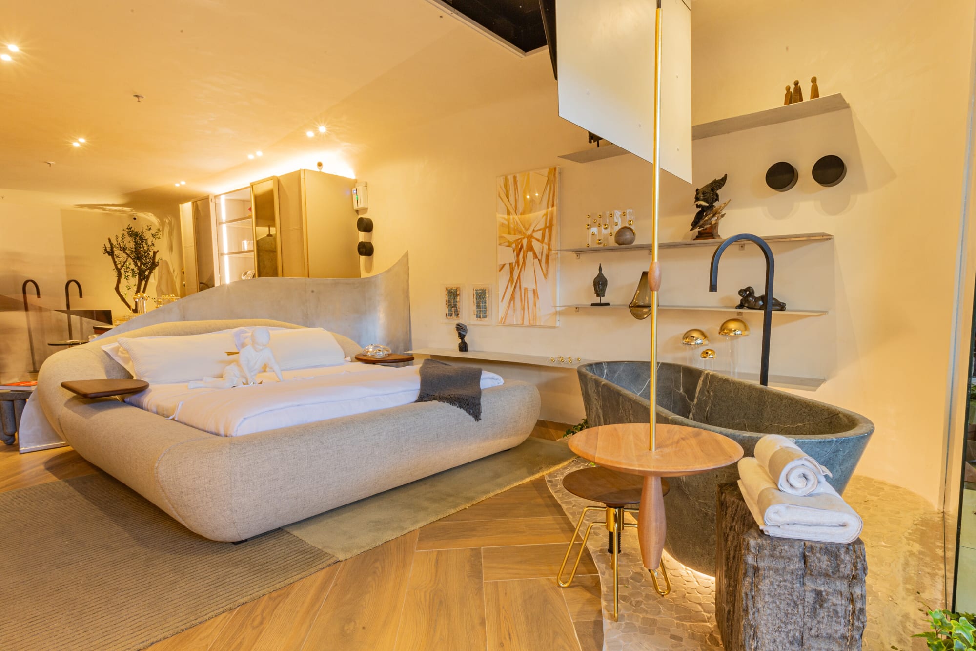 Curved bed, dark stone bathtub and floor standing tap on a herringbone timber floor