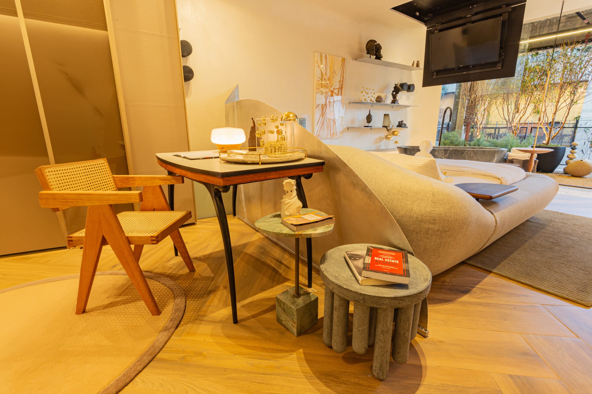 Cane writing desk and chair beside a curved bed and small round side tables