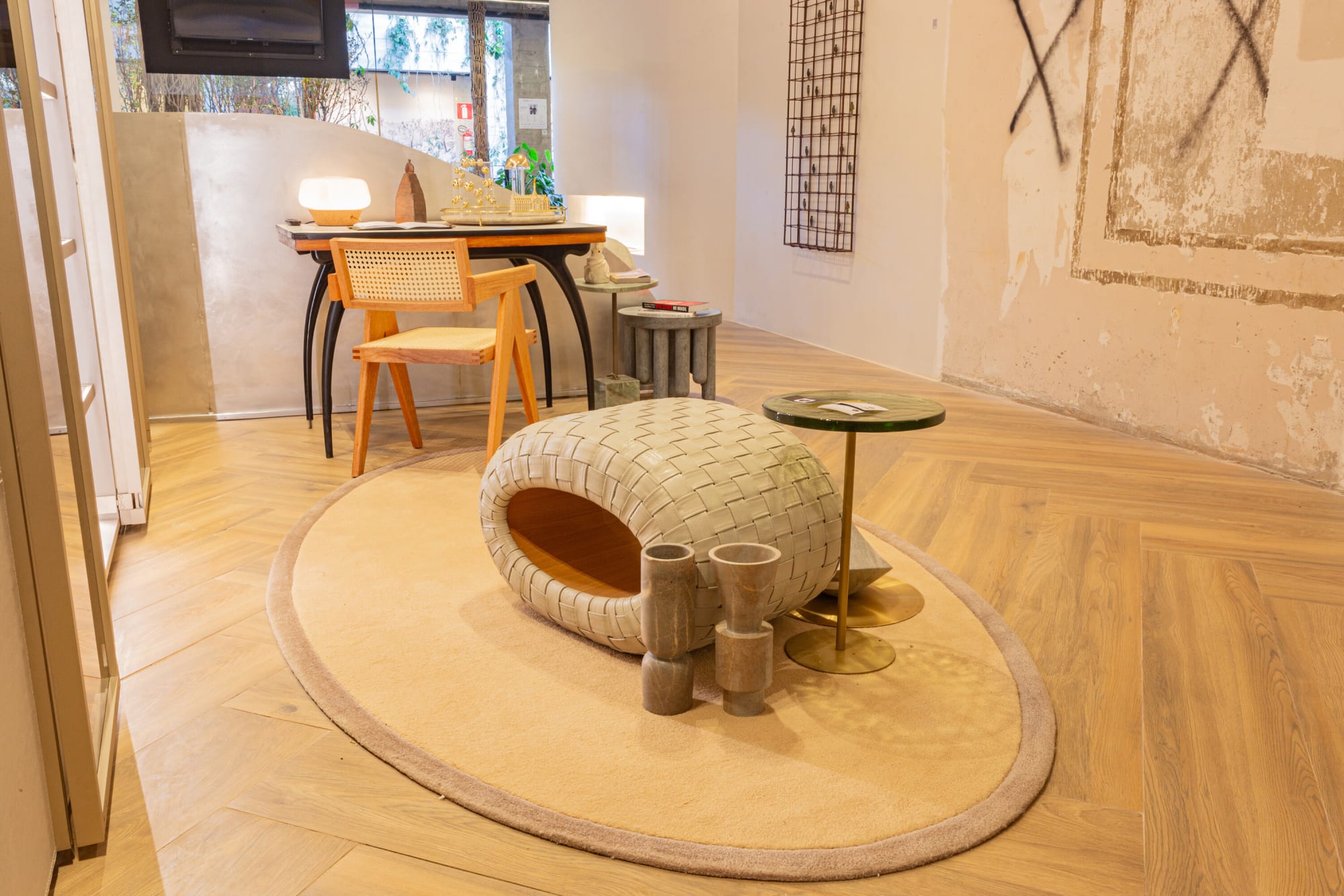 Woven ottoman on a round rug with a cane desk and grid art in a plaster suite