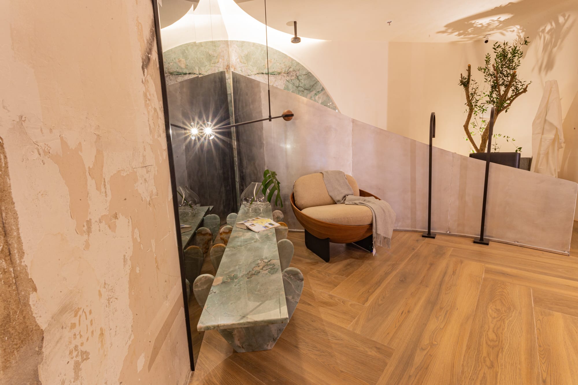Green marble bench and a lounge chair beside a mottled plaster wall and spot lights