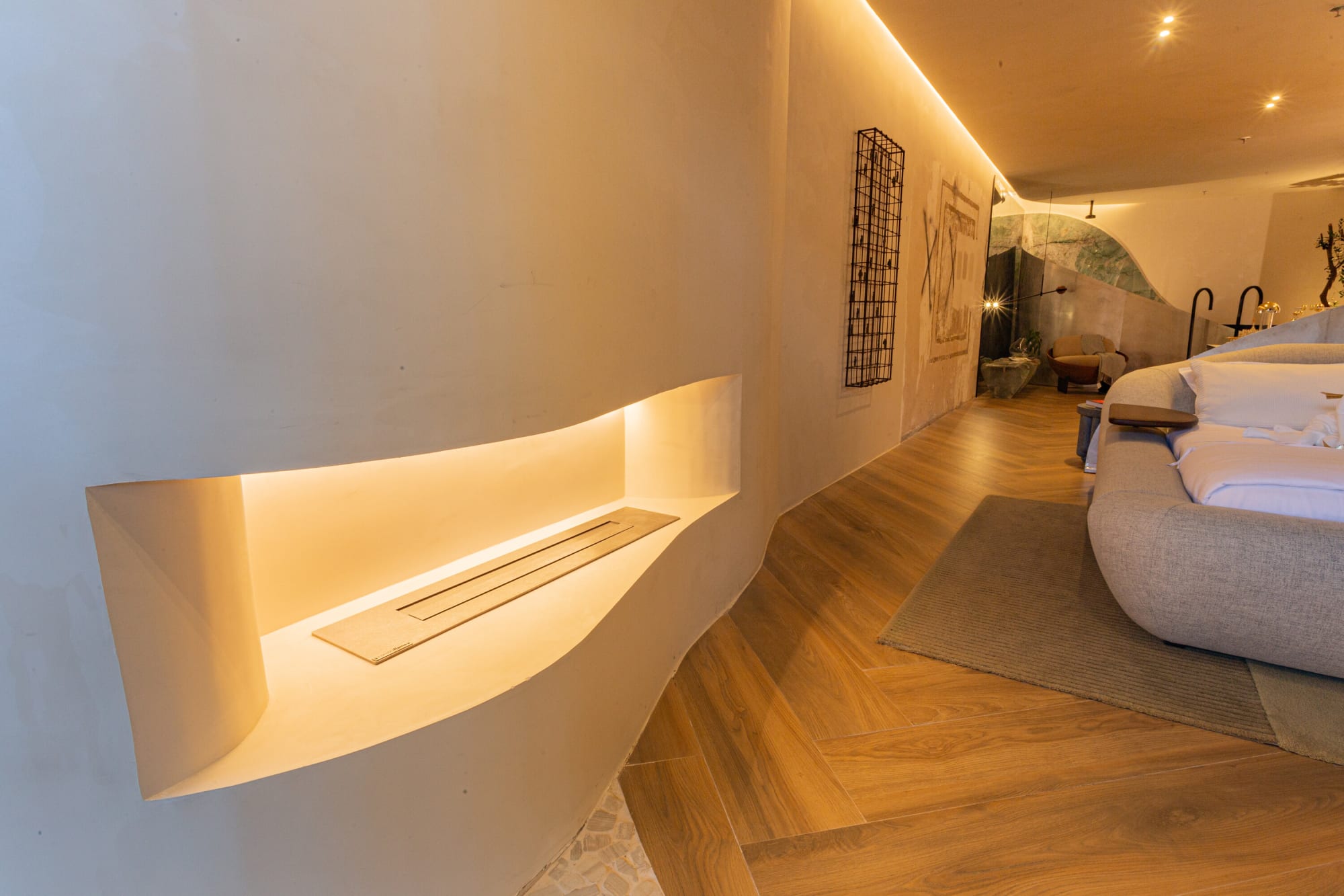 Curved plaster wall with a lit fireplace niche beside the bed on a herringbone floor