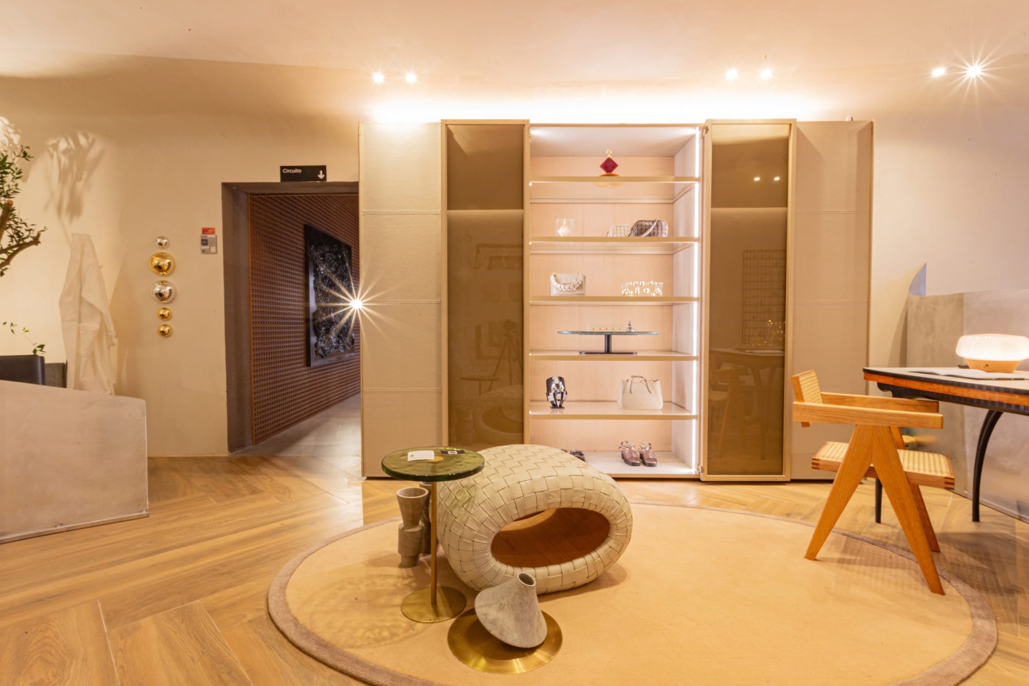 Lit glass display cabinet, round rug and woven ottoman in the CASACOR suite