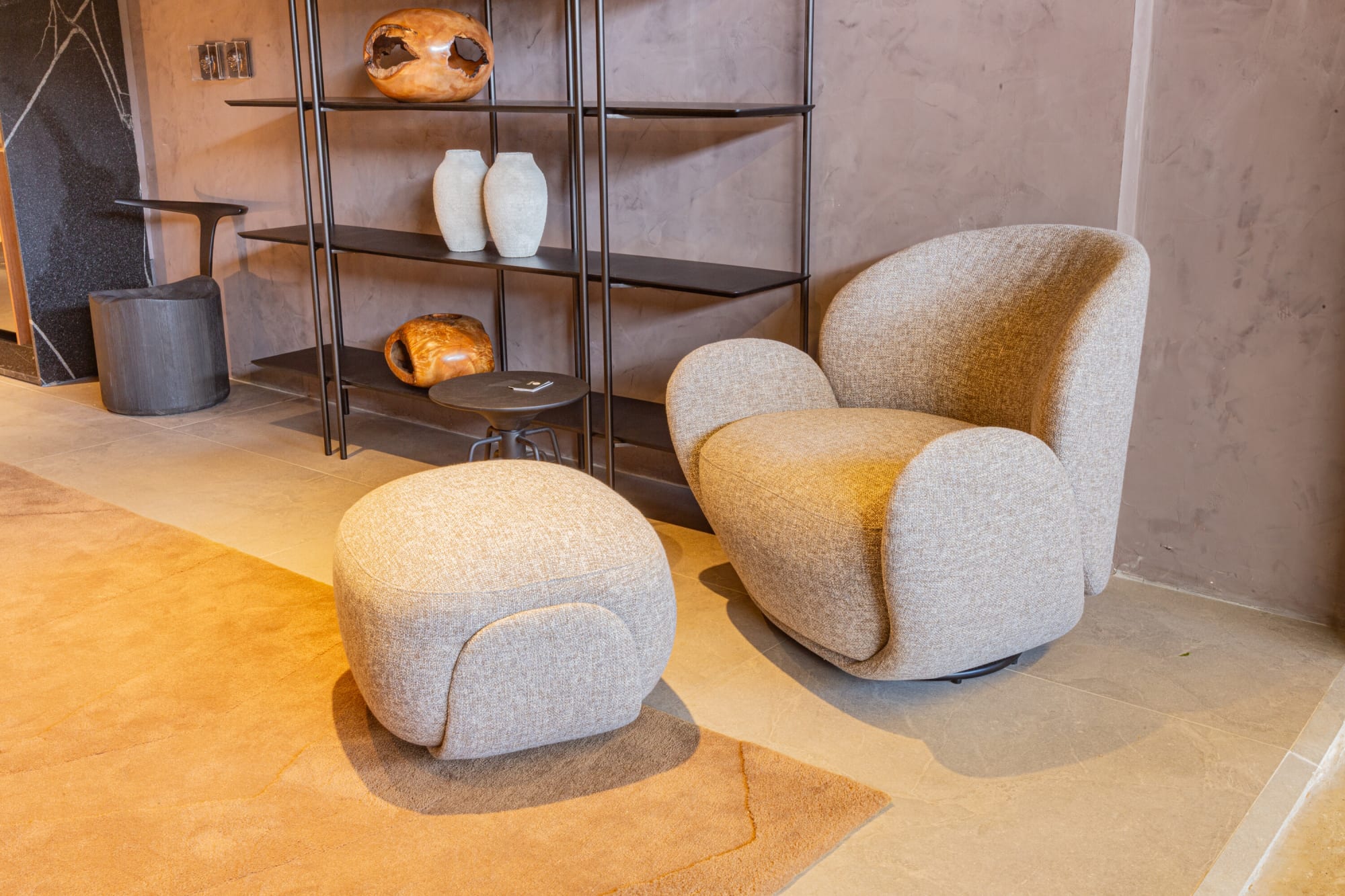 木の器を並べた黒い金属の棚の前、ブークレの回転アームチェアとプーフ