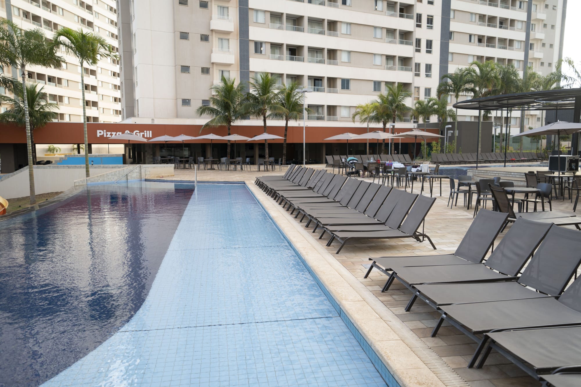 Lap pool lined with grey sun loungers beneath resort apartment towers