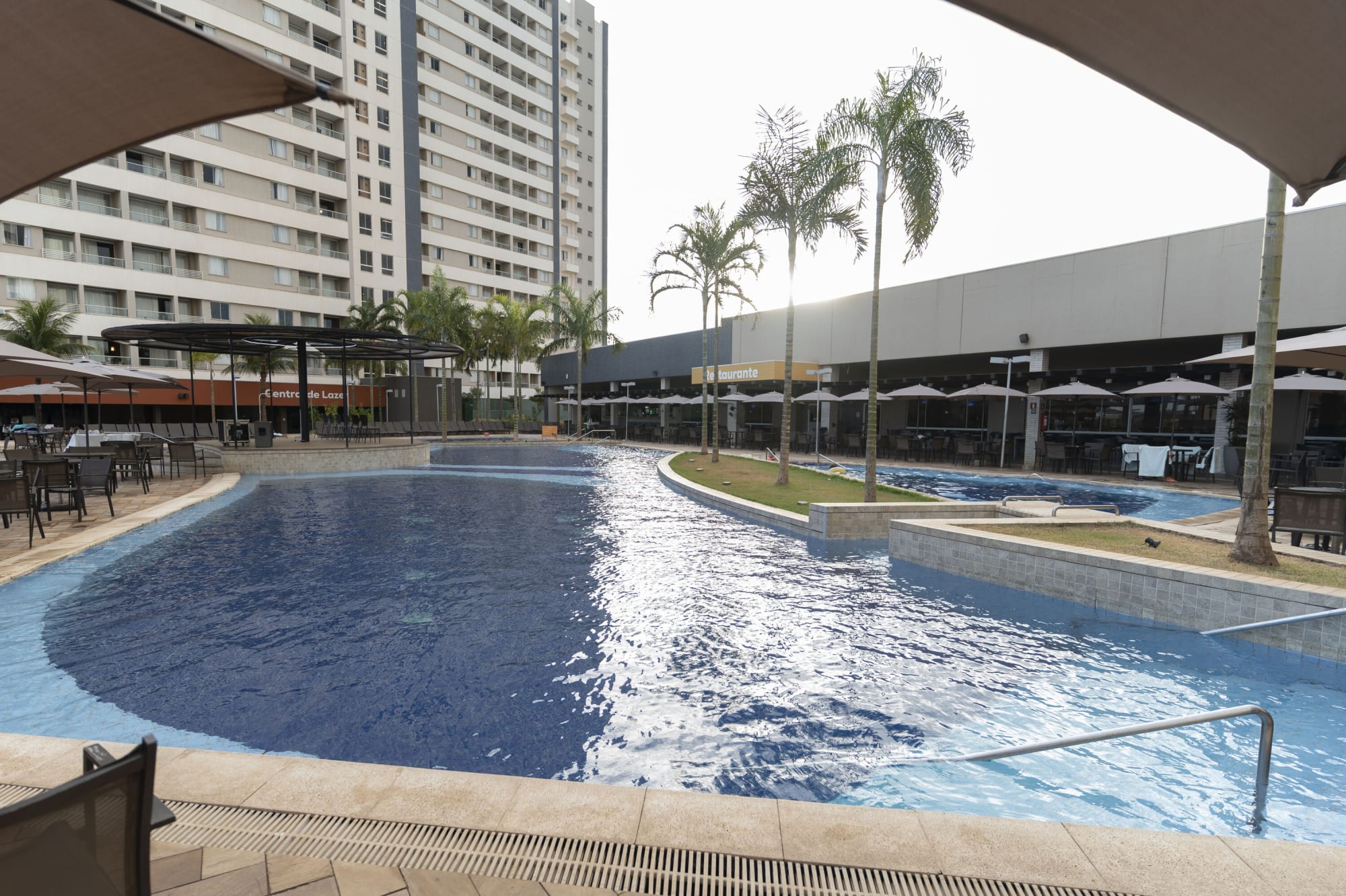Wide resort pool with shade sails, palms and restaurant terrace