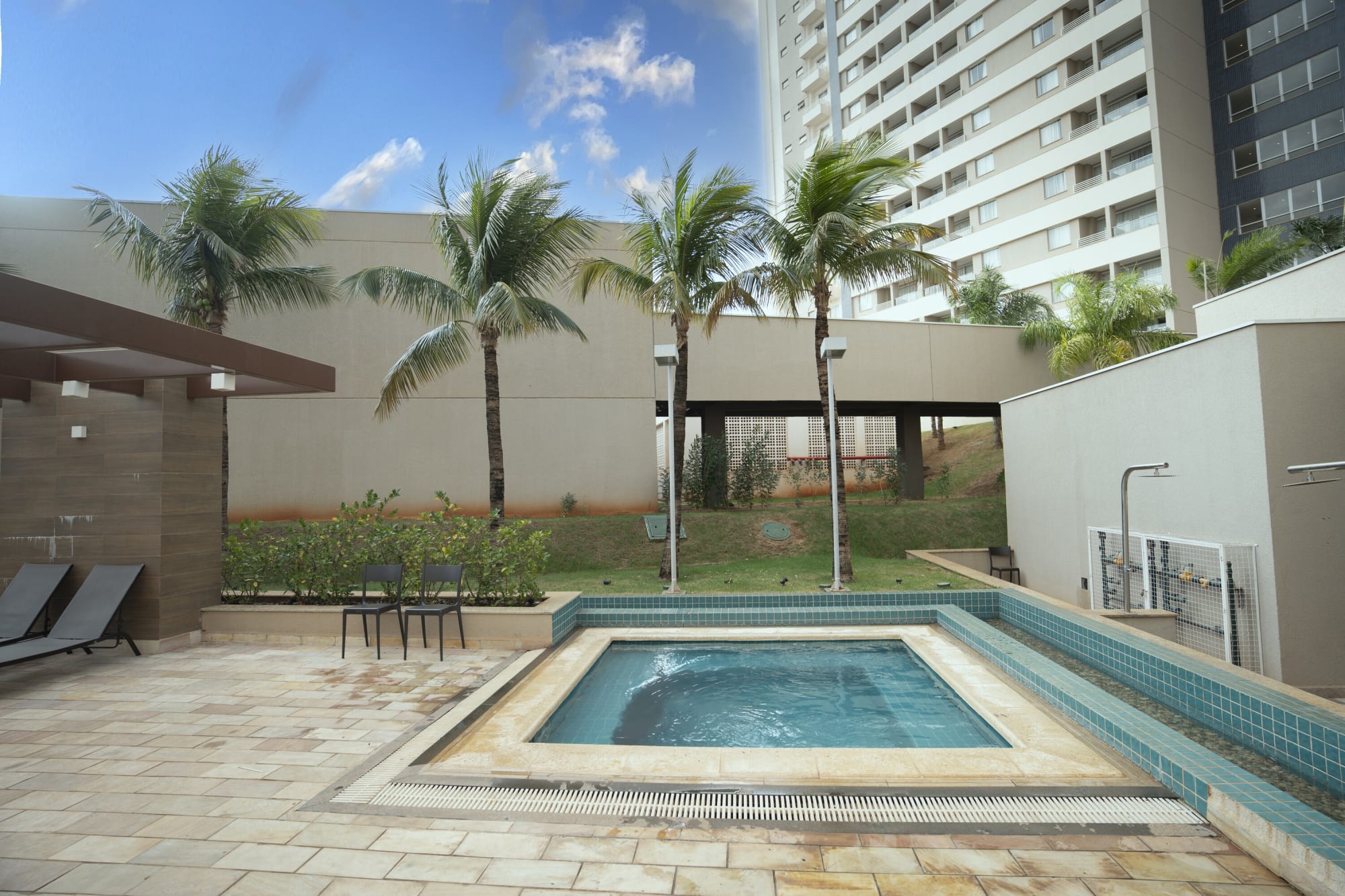 Small tiled hot tub on a stone terrace with palms and grey loungers