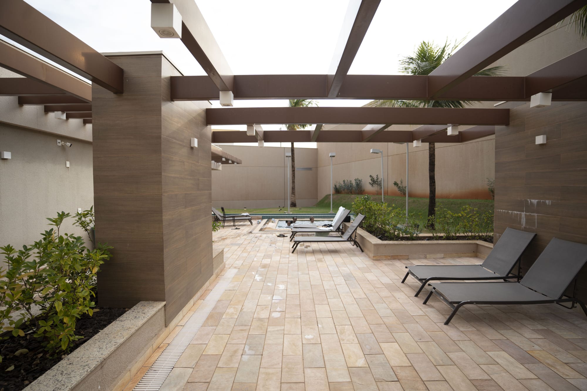 Timber pergola walkway over stone paving with grey sun loungers