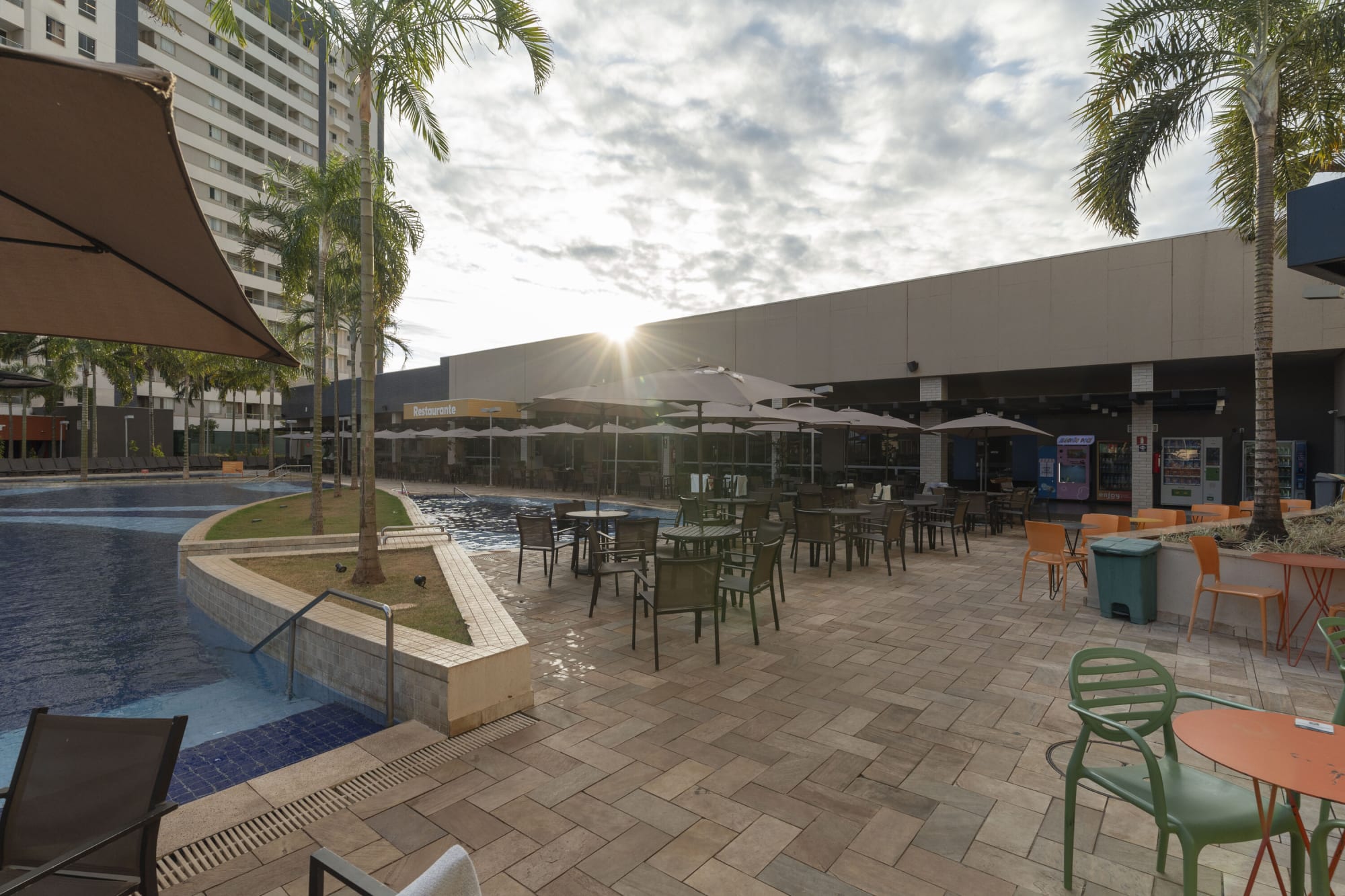 Pool terrace with green chairs and round tables under a cloudy sky