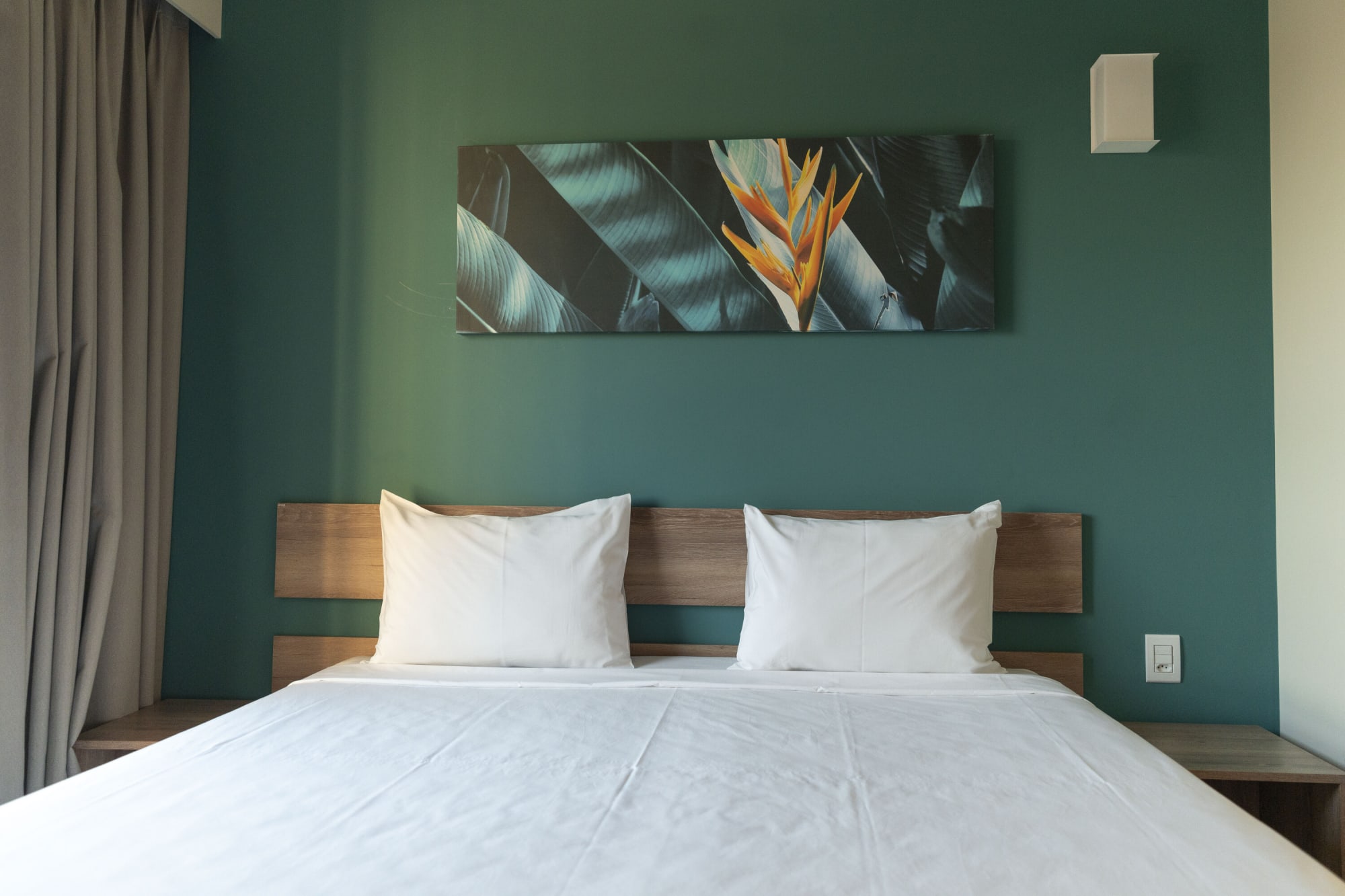 Resort room with white bed, teal wall and bird of paradise print