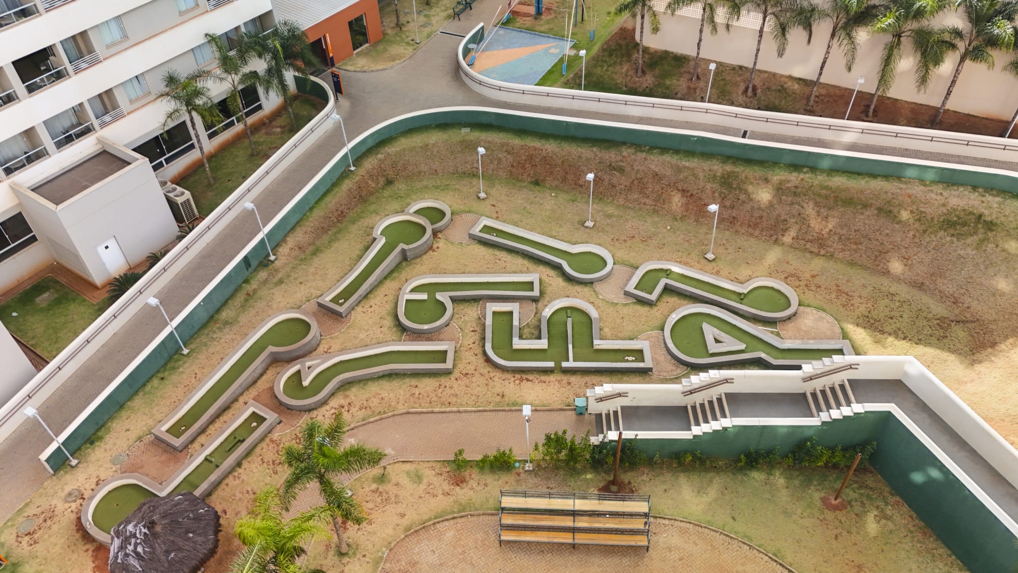 Aerial view of a mini golf course framed by green walls and palms