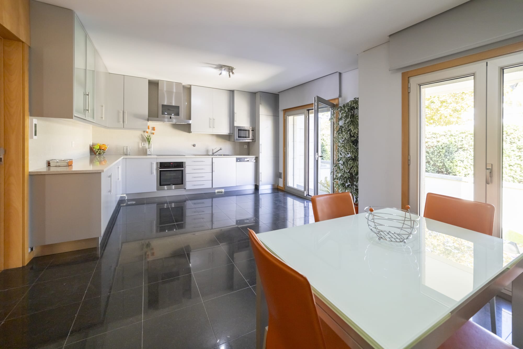 White kitchen with orange chairs around a glass table on dark tiles