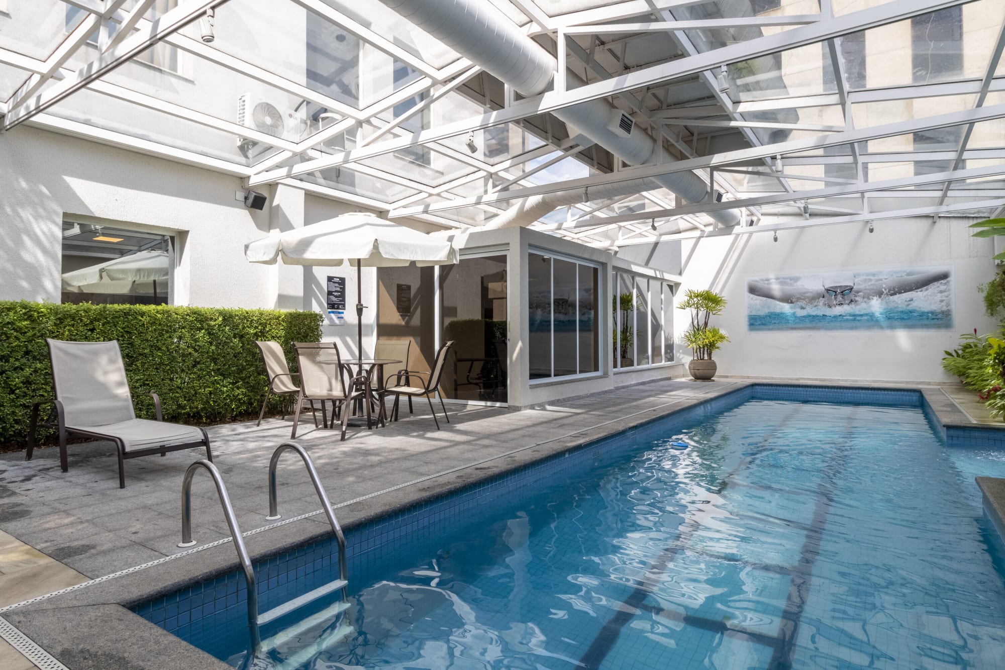 Glass roofed pool with white loungers, patio table and parasol