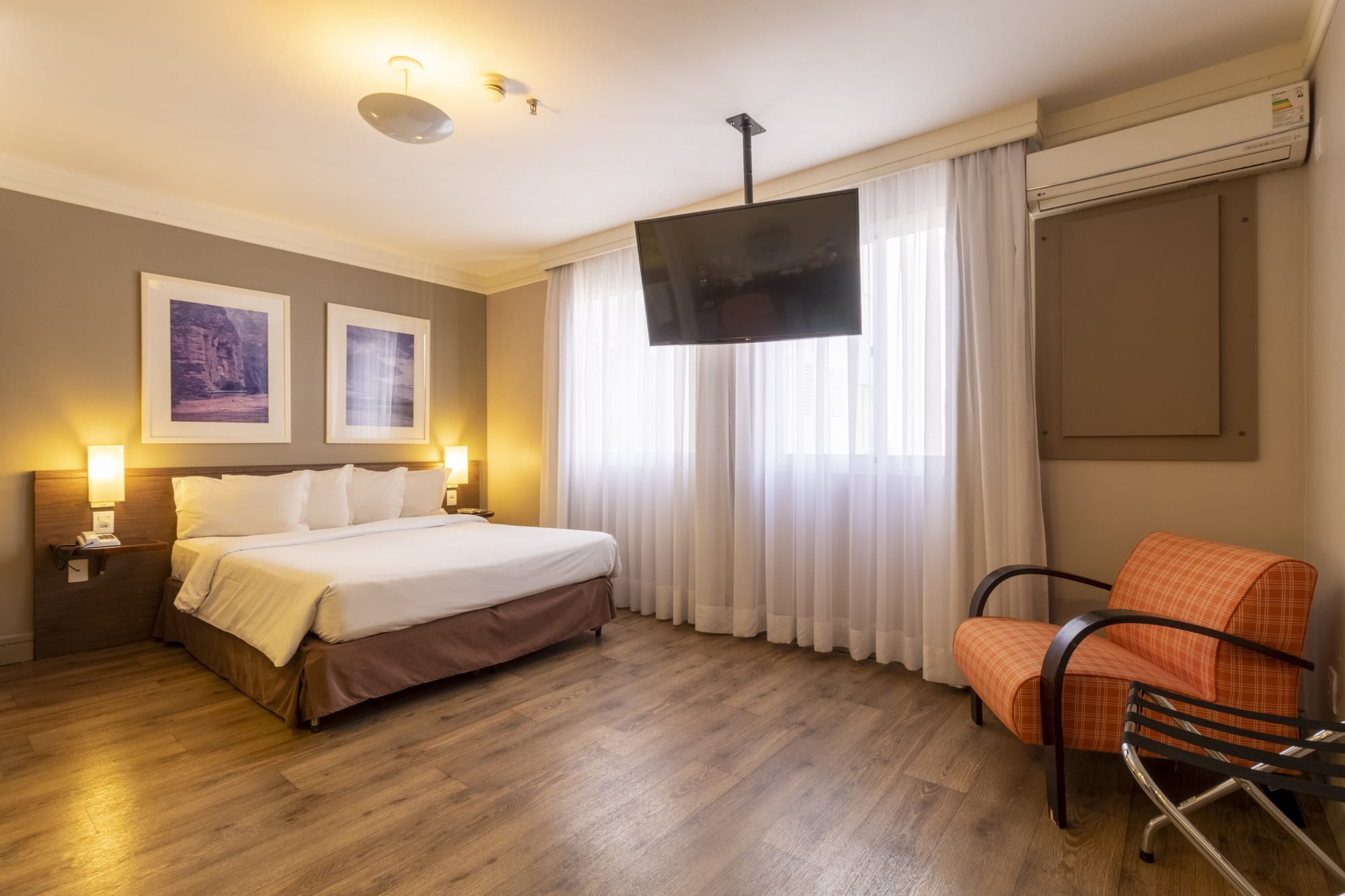 Hotel room with white bed, orange armchair and ceiling mounted television